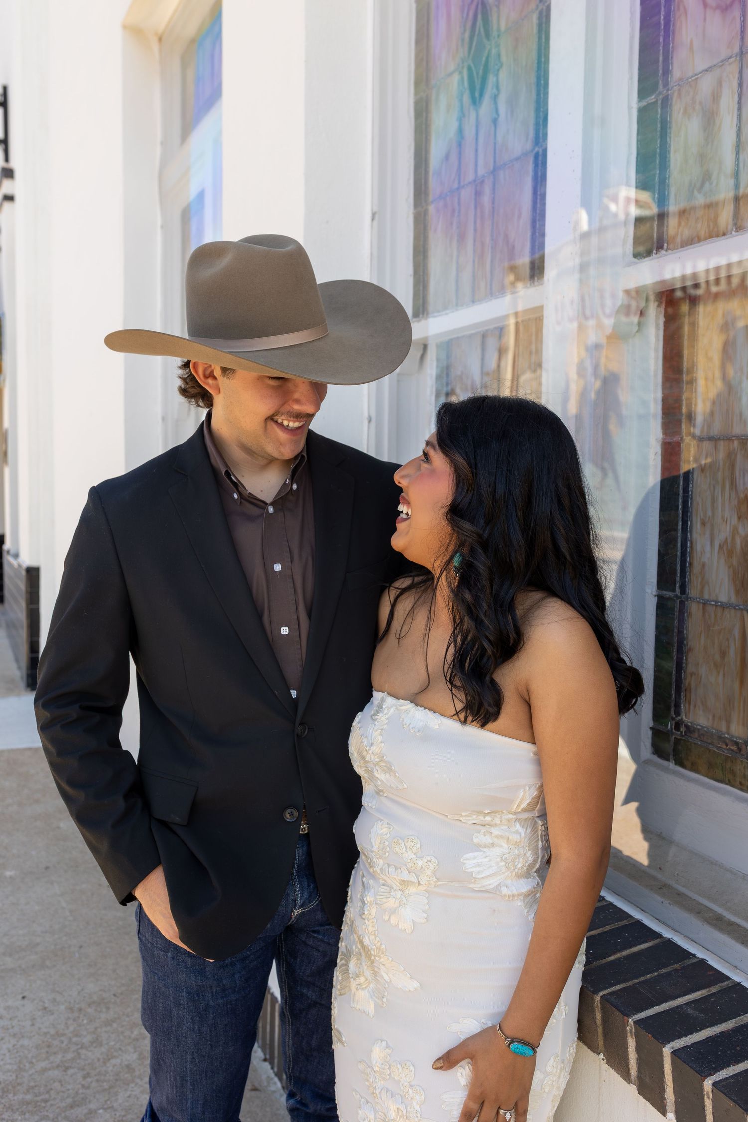 A couple in western wedding attire share intimate moments against a colorful wall backdrop.