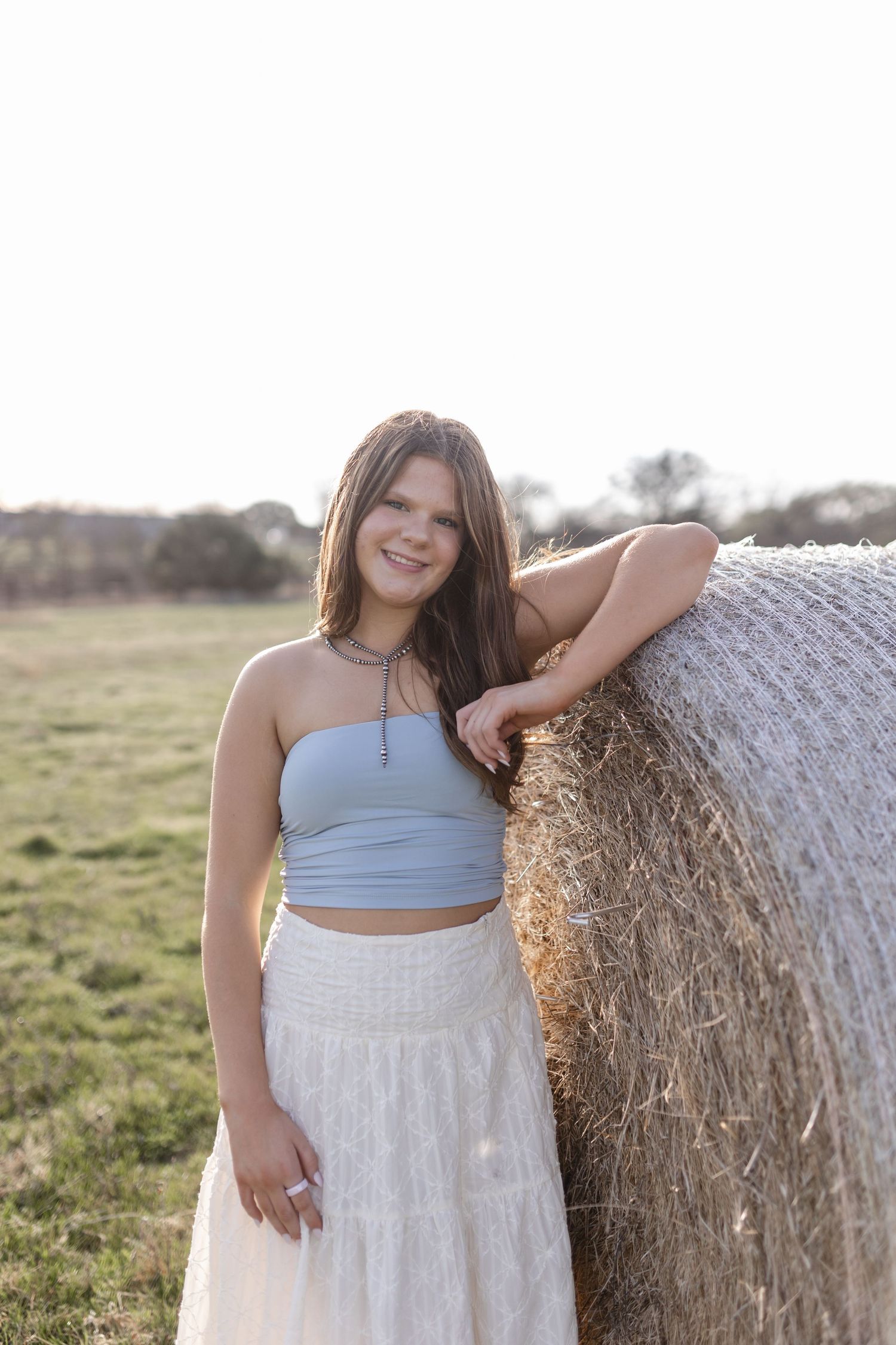 Rural countryside portrait session with hay bales featuring a light blue crop top and white lace skirt ensemble.