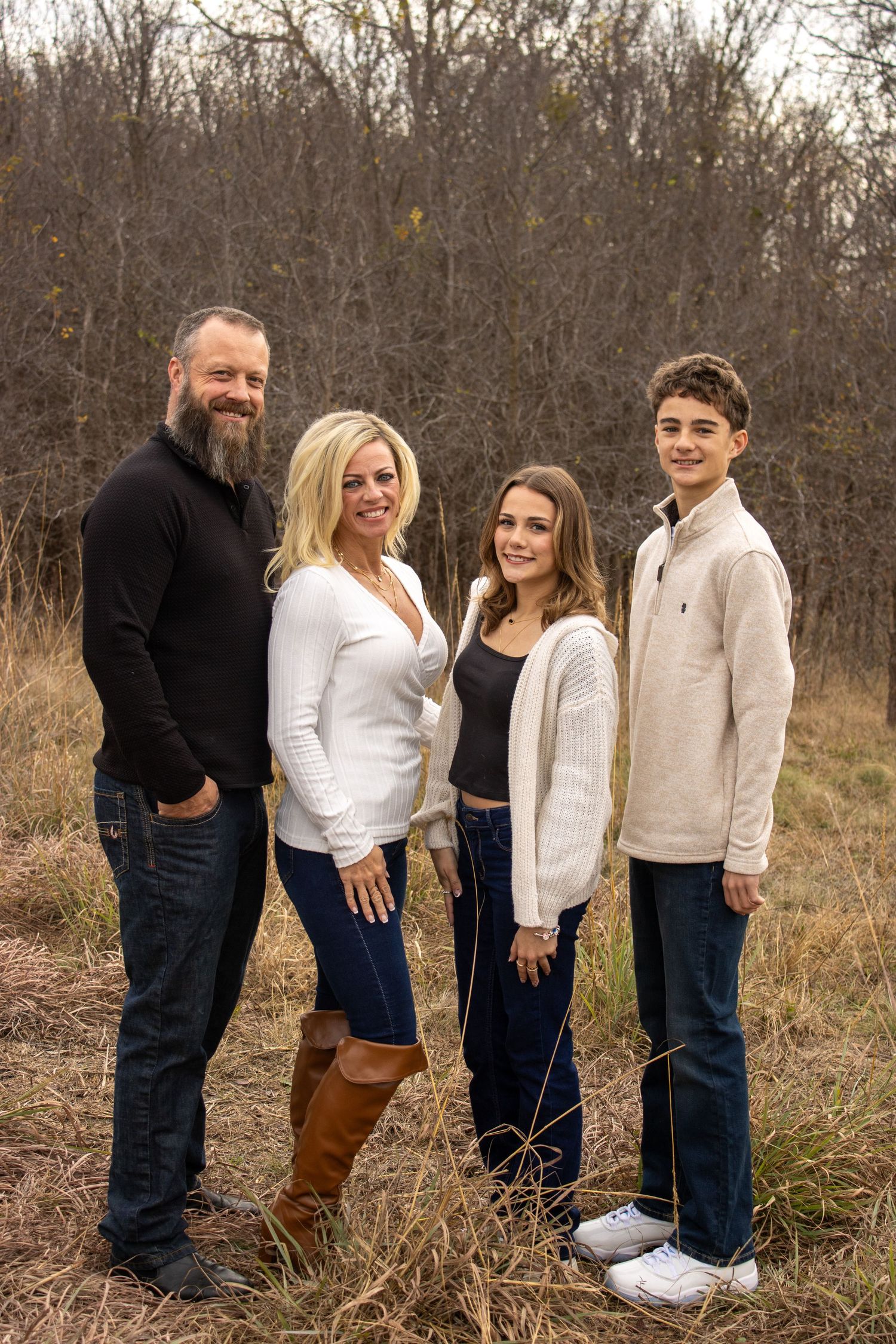Family in coordinated white and neutral outfits poses together in a rustic outdoor setting with tall grass and trees.