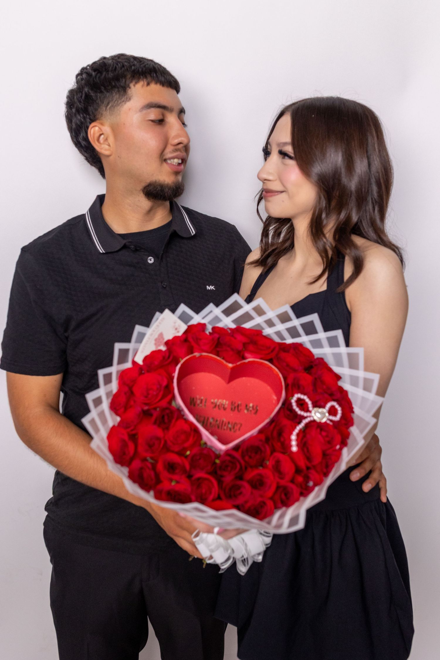 A couple holds a beautiful red rose bouquet with a heart-shaped centerpiece wrapped in white decorative paper.