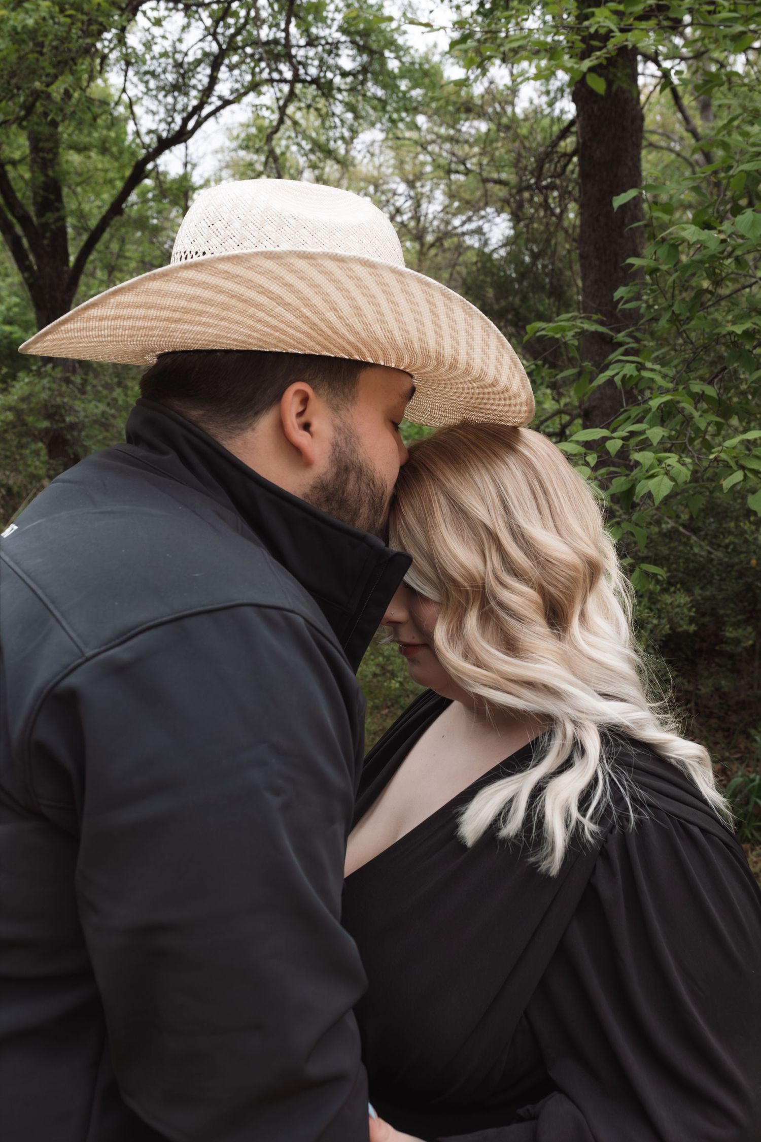 A romantic couple in black clothing sharing intimate moments in a wooded outdoor setting.