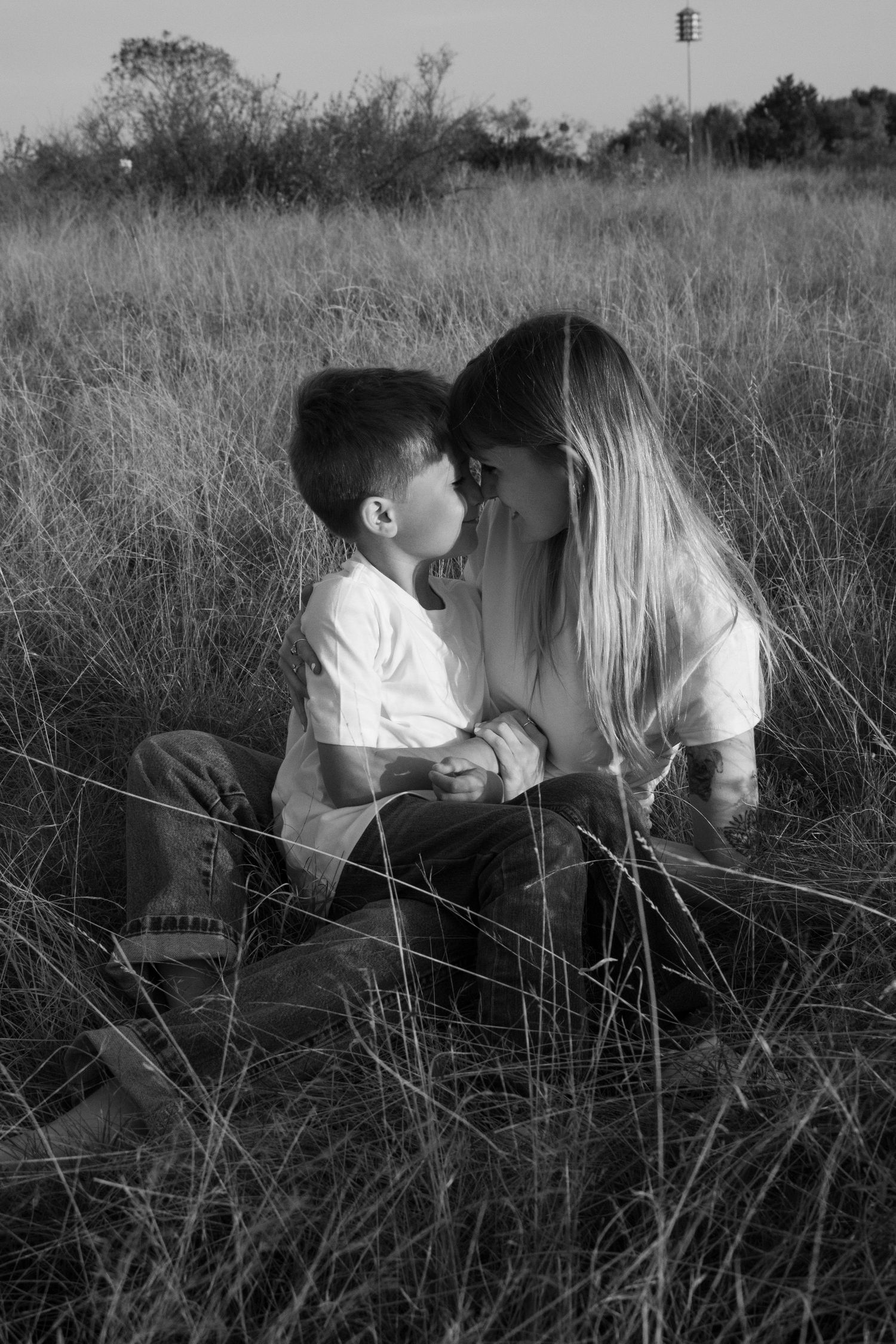 Black and white photo of tender moments shared between parent and child in a grassy field at sunset.