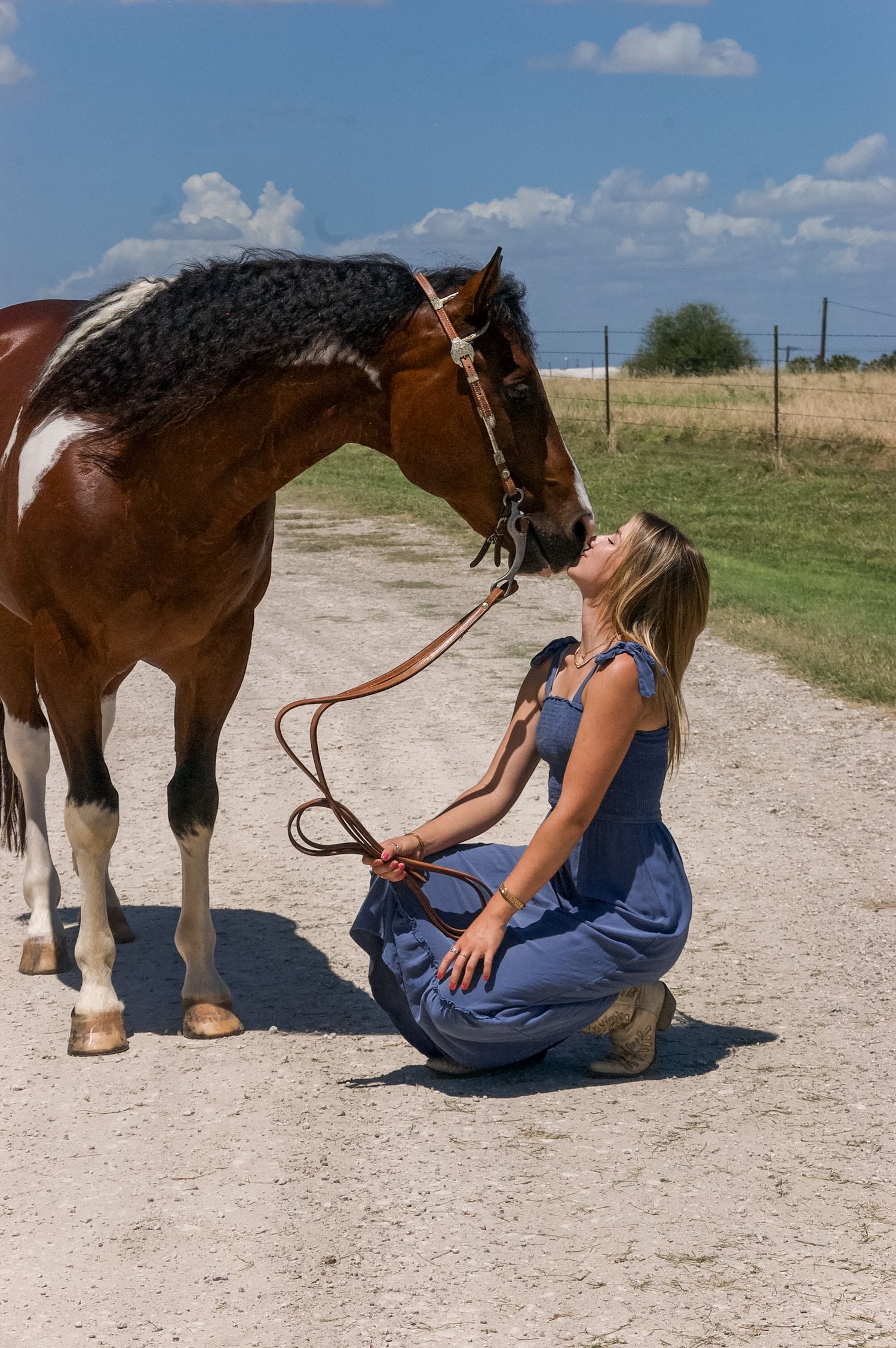 Person sitting on ground bonding with brown and white horse outdoors.
