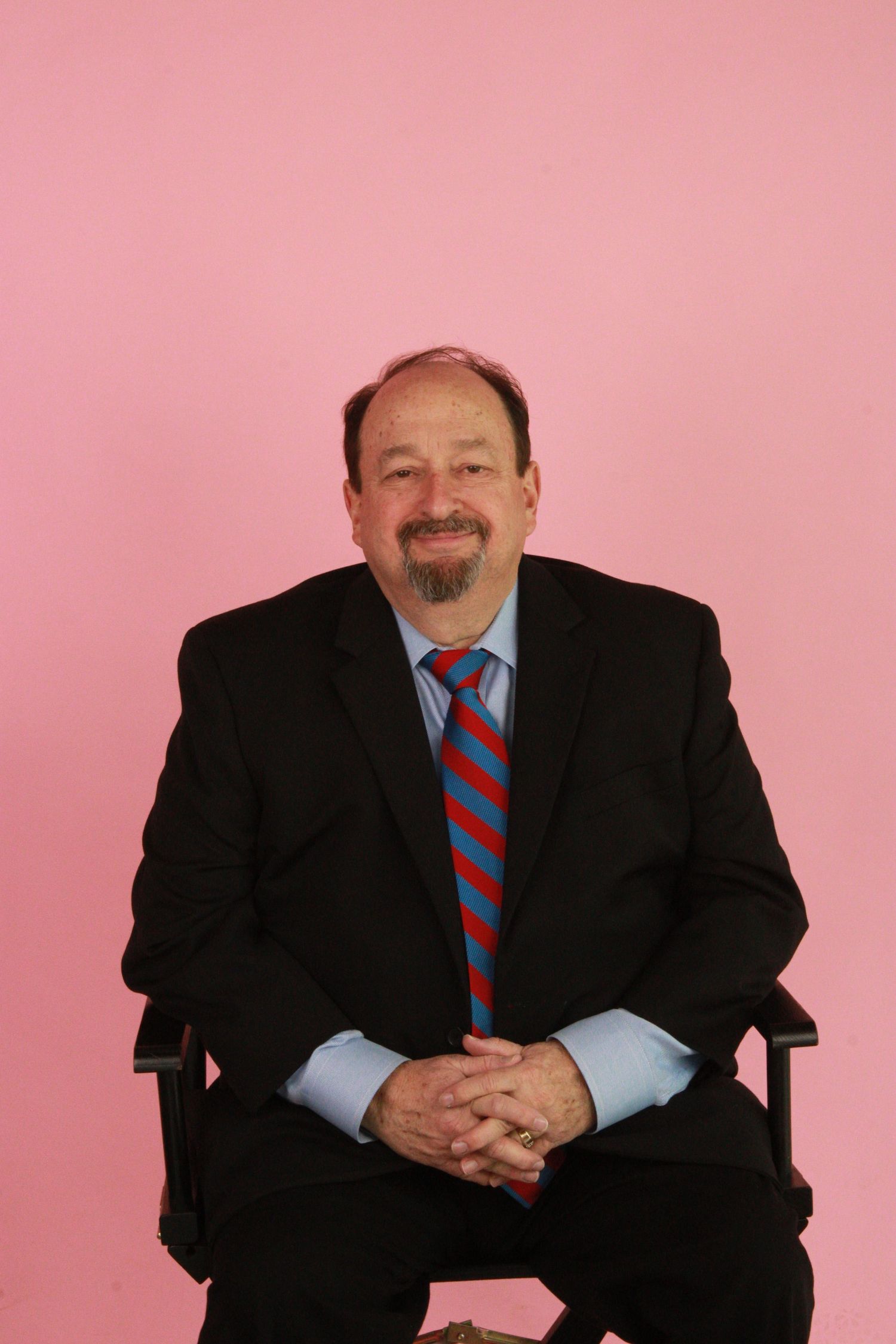 Professional headshot series against pink background showing person in black suit and striped tie in various poses.
