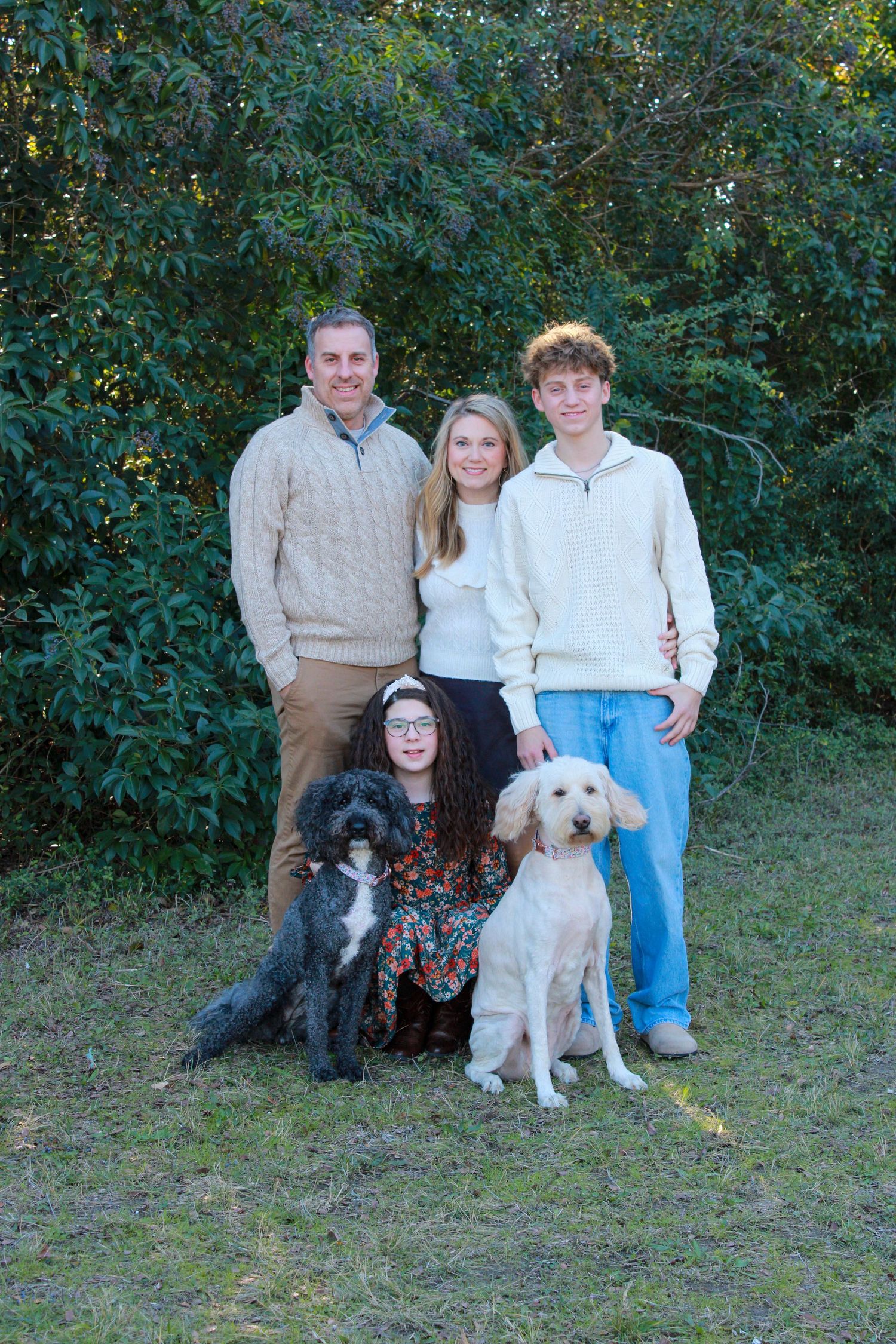 A family poses outdoors with their black and white dogs against a green foliage background.