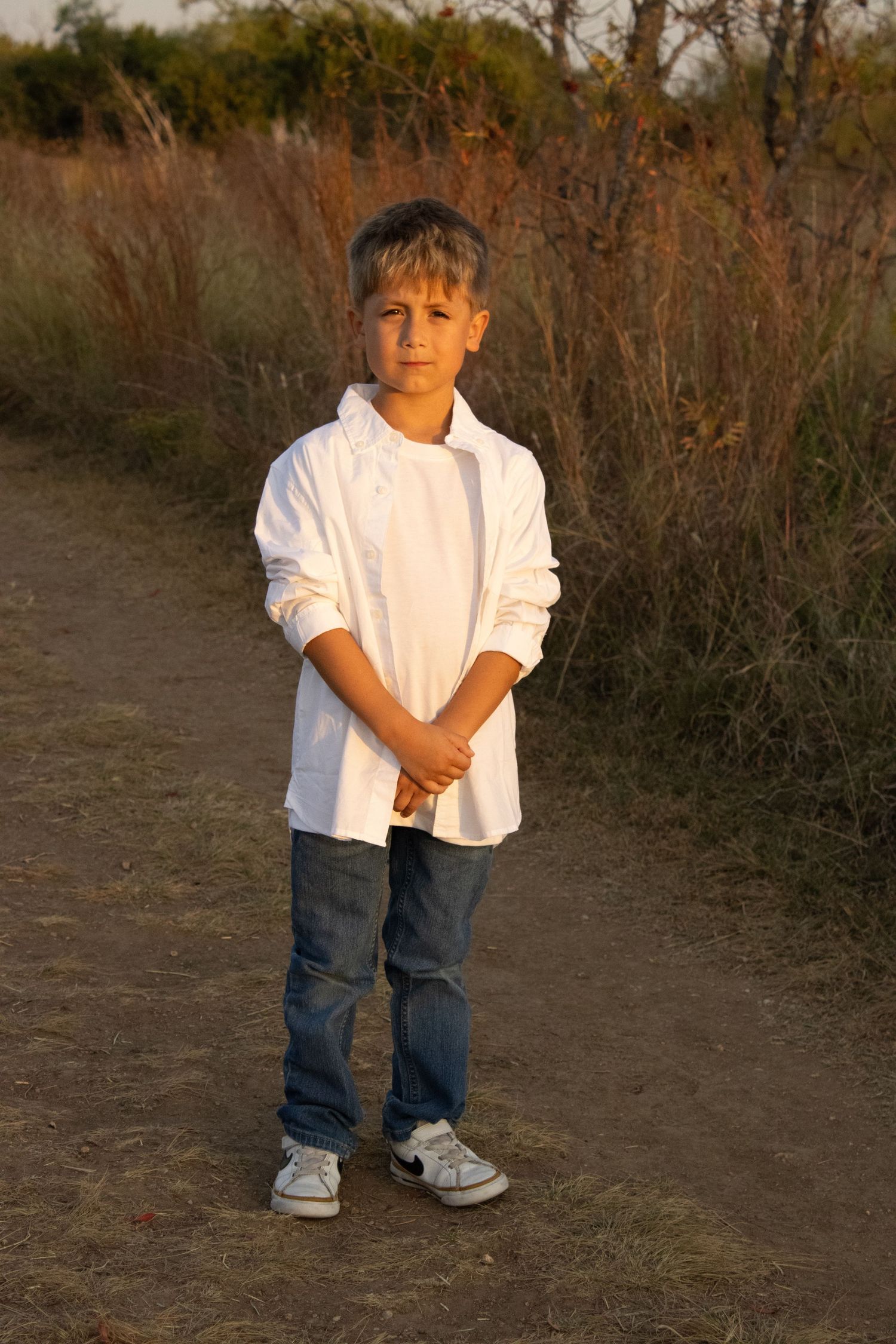 Young child in white shirt and jeans standing on a dirt path during golden hour.