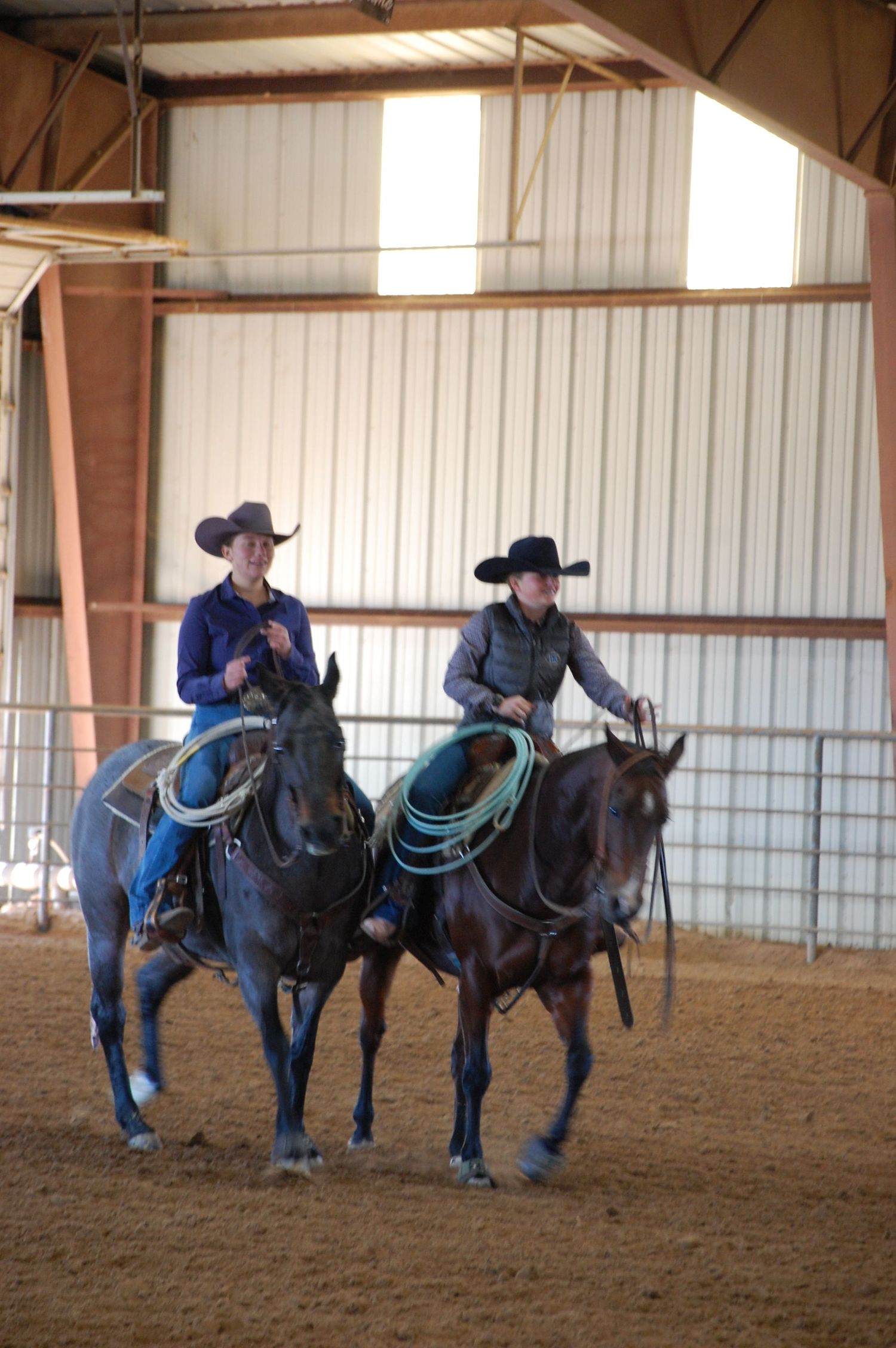 Multiple riders practicing with their horses in an indoor riding arena.