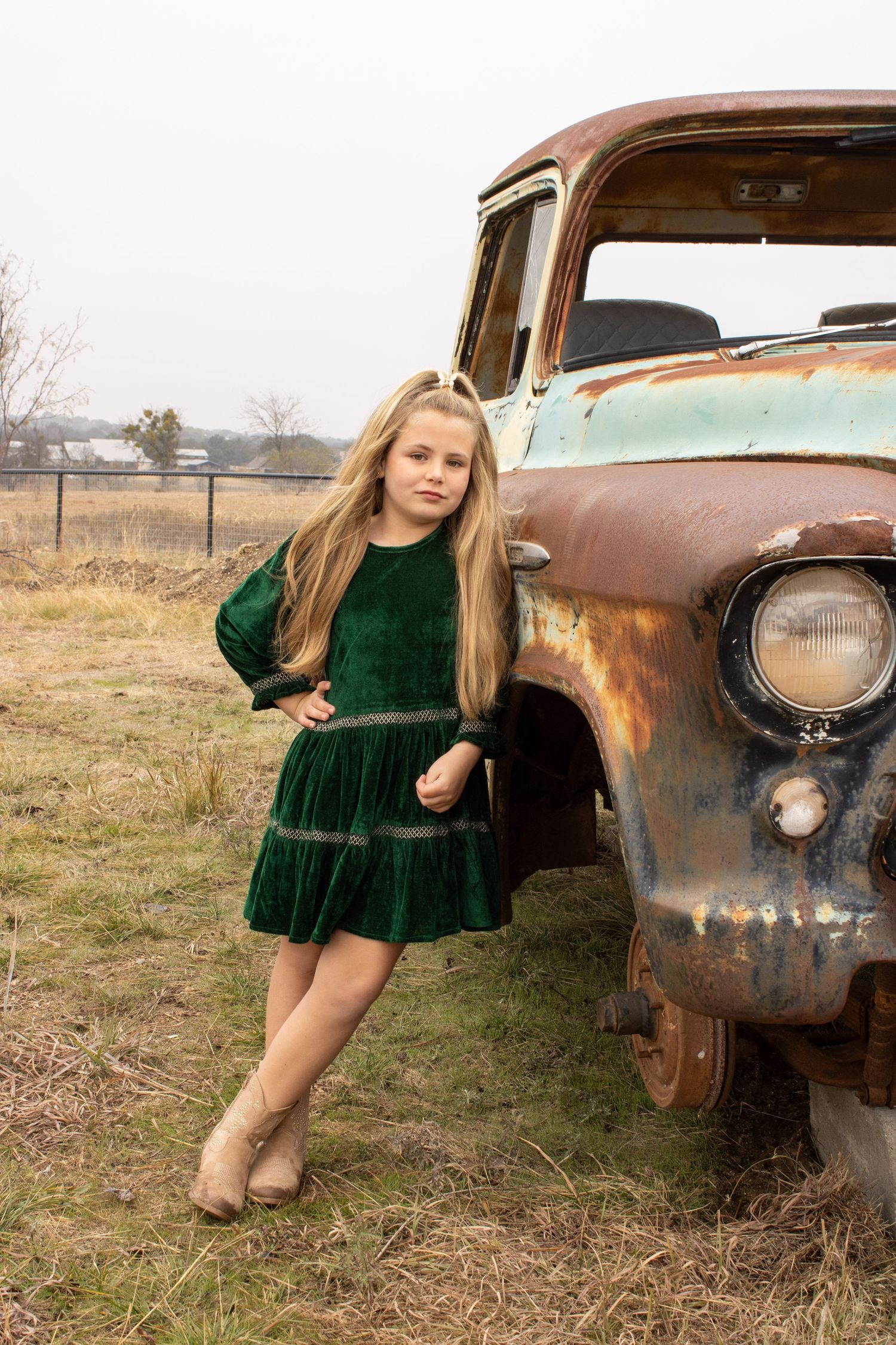 A rustic photoshoot featuring an old rusty vintage car in a grassy field with soft natural lighting.
