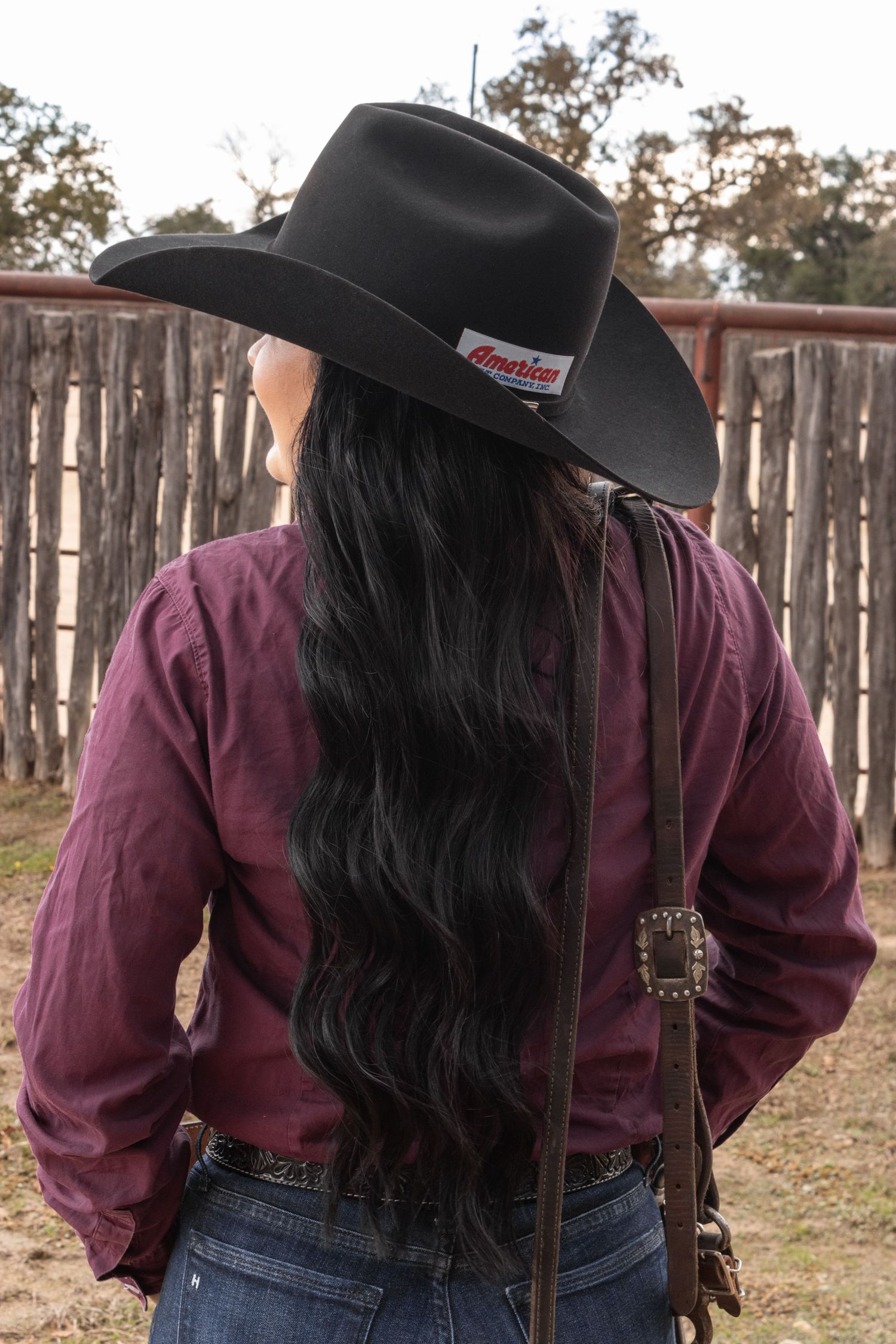 Person wearing a maroon shirt and black hat shown from behind against a wooden fence background.