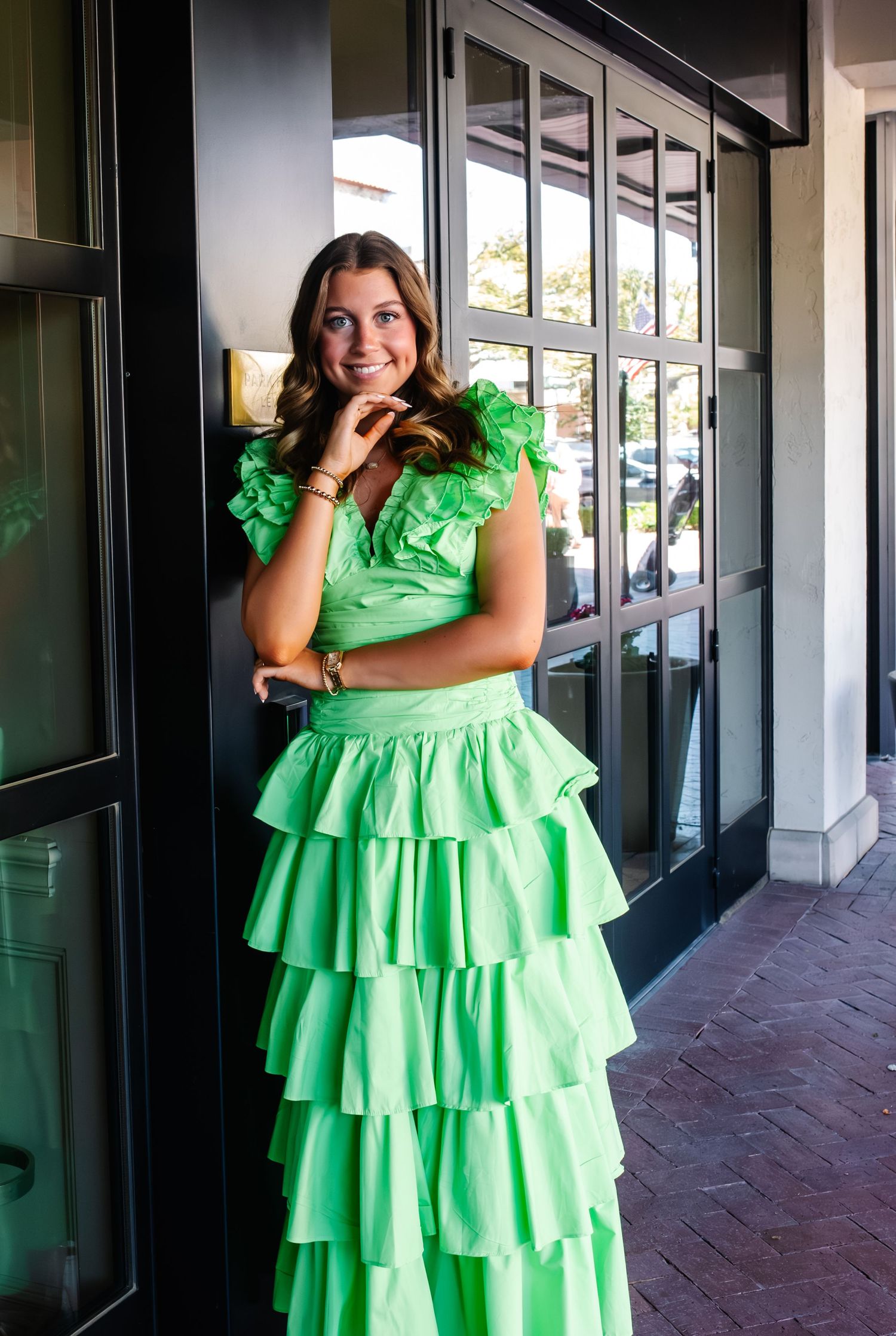 A bright lime green tiered ruffle dress photographed in an outdoor covered walkway with dark columns.