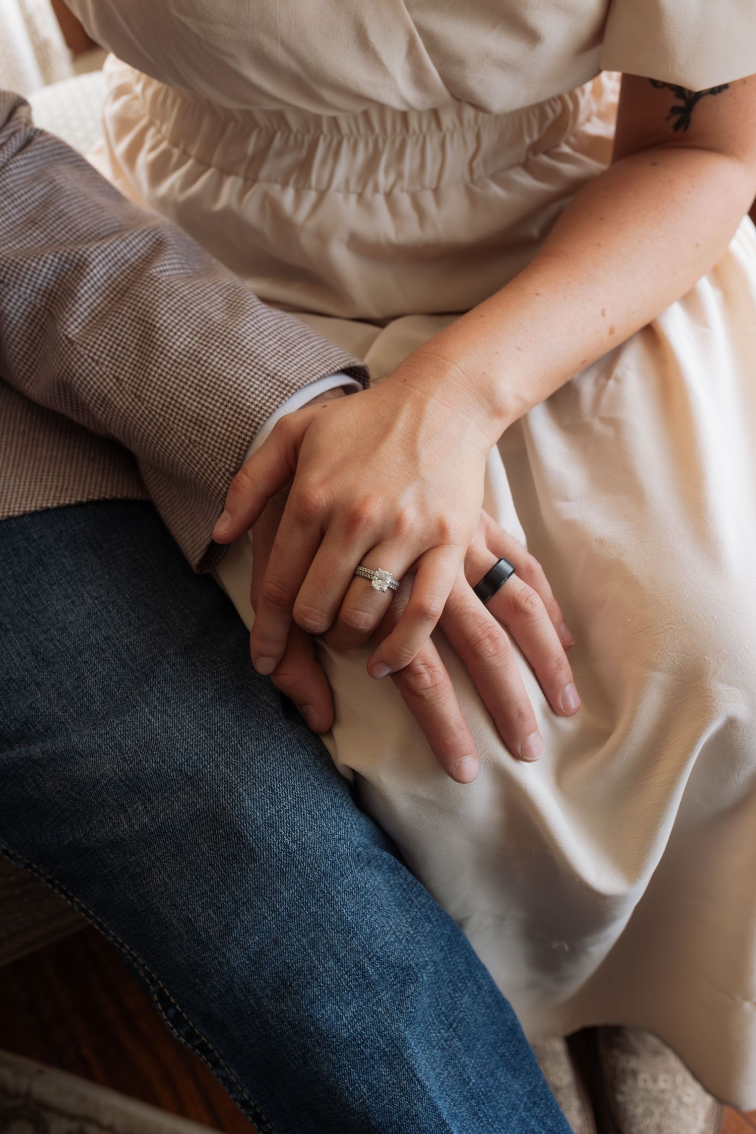 Close-up of a couple holding hands showing engagement ring and wedding band while sitting together.