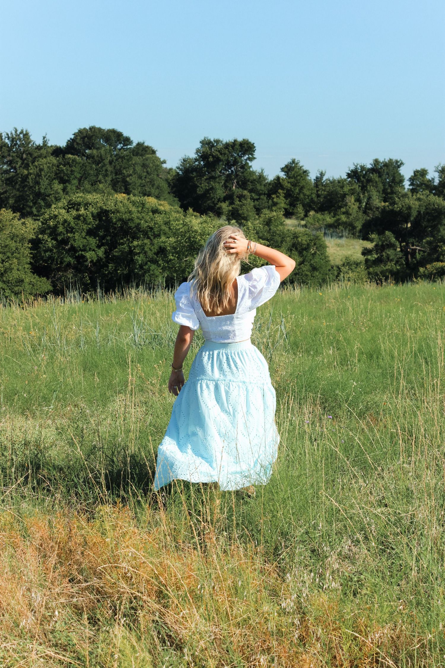Person in blue dress walking through tall grass field on sunny day.
