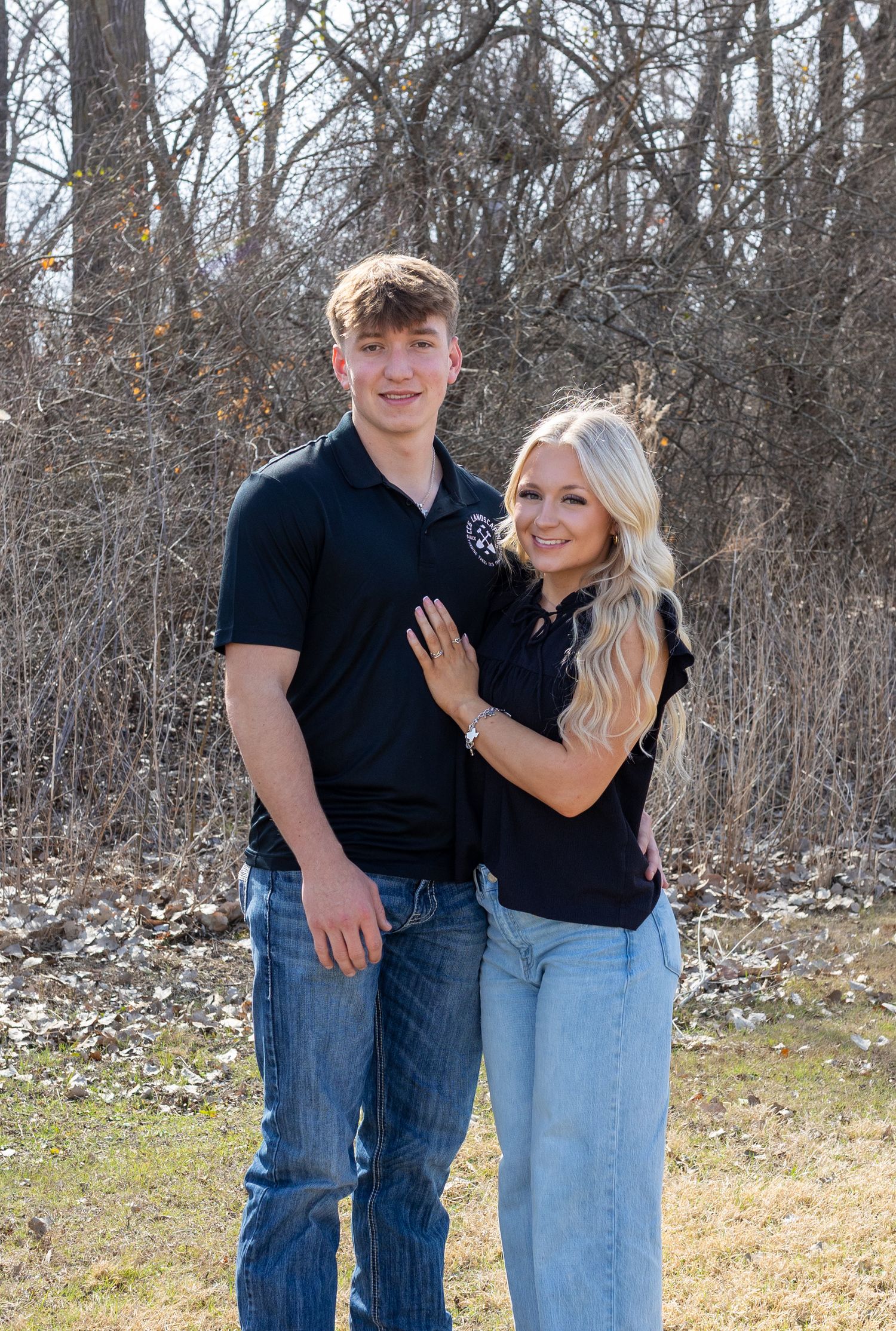 Casual couple posing outdoors against a backdrop of bare winter trees.