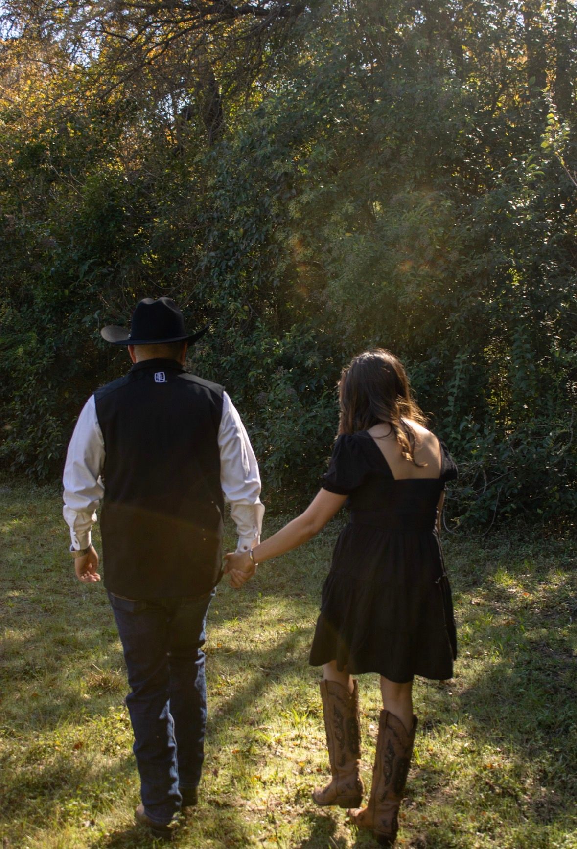A couple in vintage clothing walks together through a sunlit wooded area during autumn.