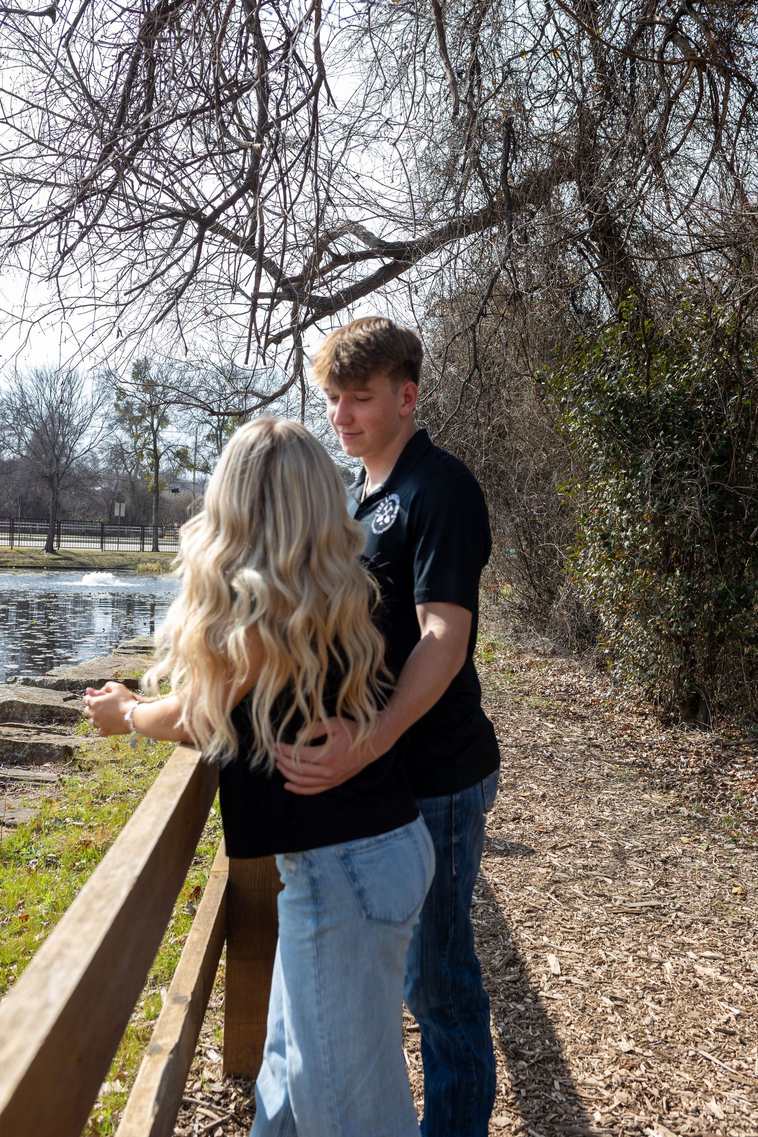 A couple shares an intimate moment by a lake while standing near a wooden railing.