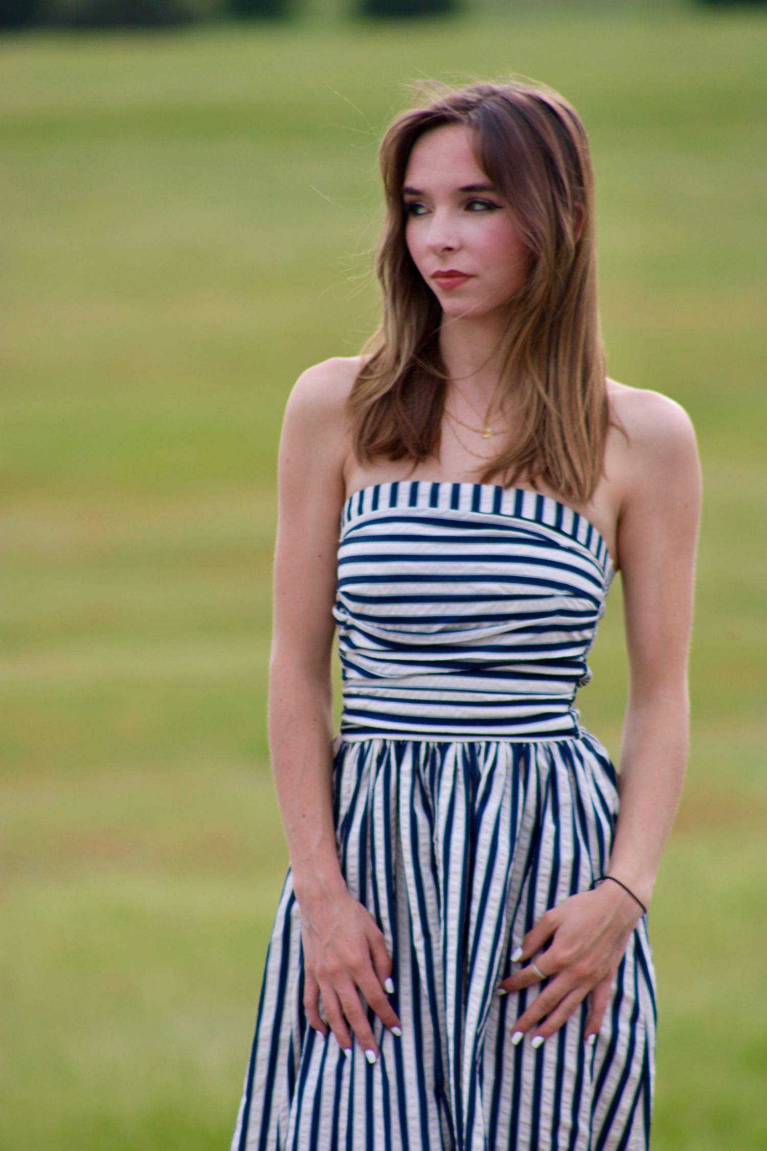 Person wearing a striped sundress poses in a grassy field.