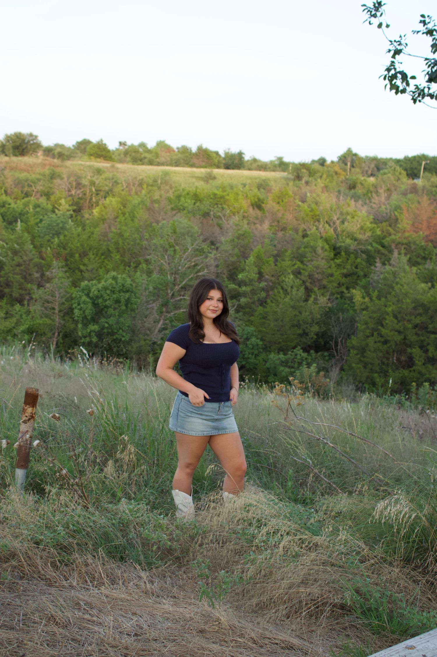 Woman in casual attire poses in a grassy field during golden hour.