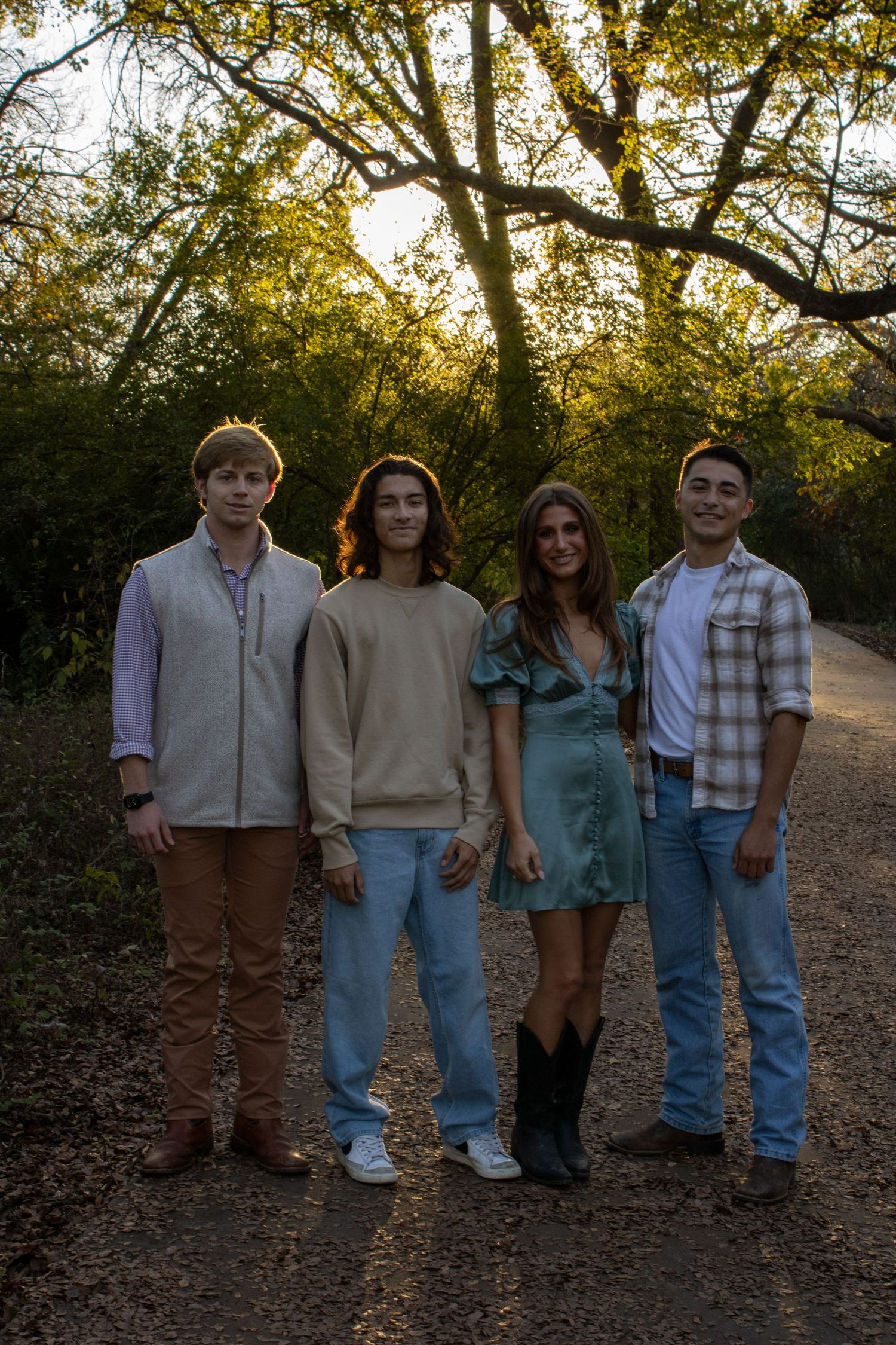A group of people standing together on a dirt path during golden hour with trees in the background.