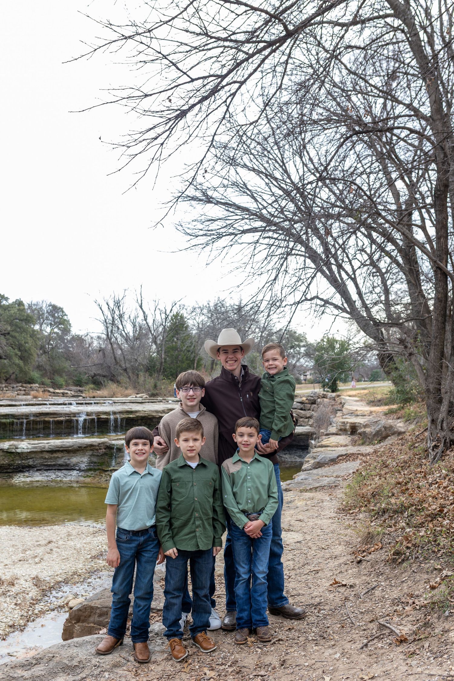 A group stands together on a dirt path near a scenic waterfall and pond on a winter day.
