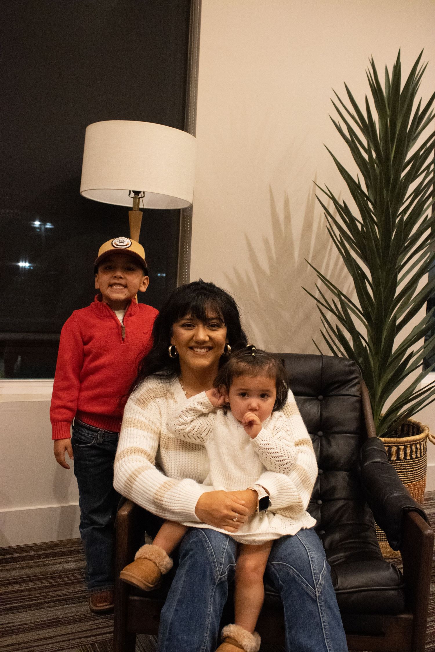 A family portrait in a living room with a tall palm plant and floor lamp creating a warm atmosphere.