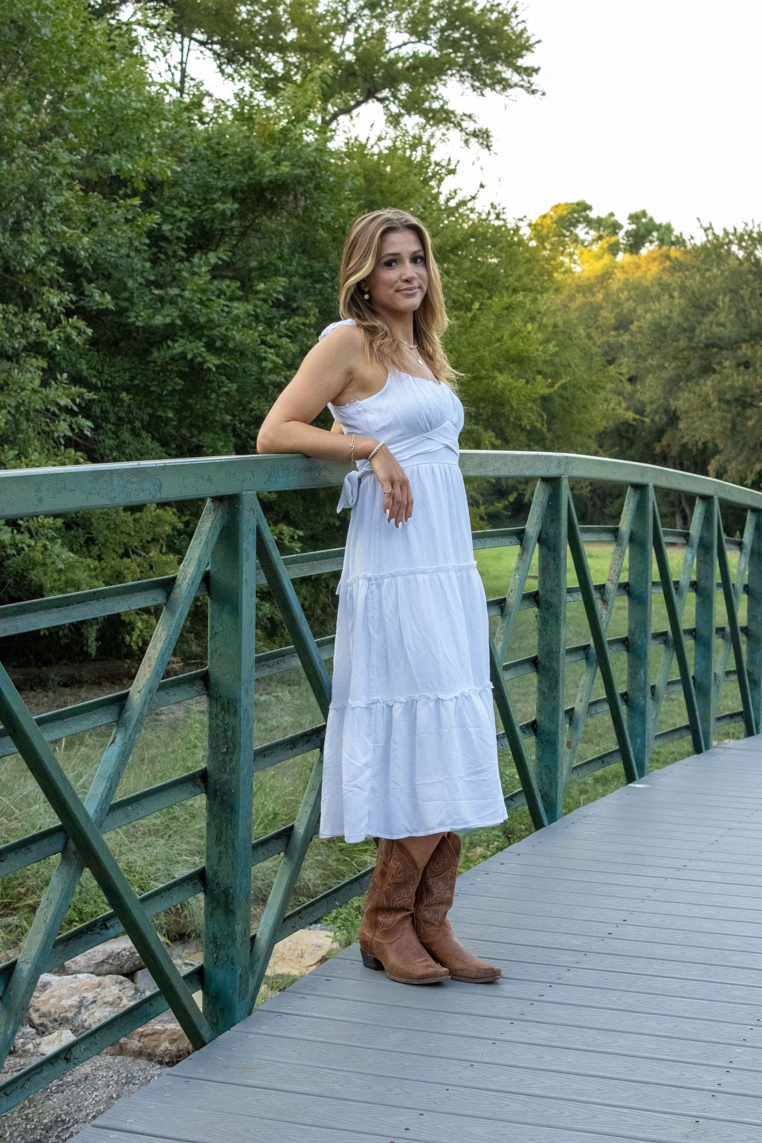 A summer portrait on a green metal bridge wearing a white dress and brown boots.