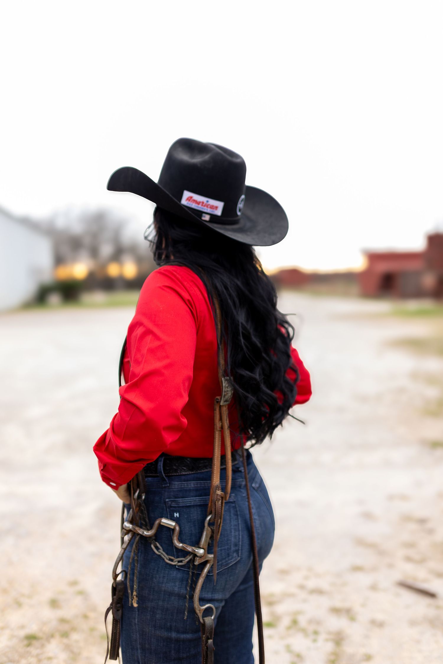 A person in a black cowboy hat and red shirt walking along a dusty path in western-style attire.