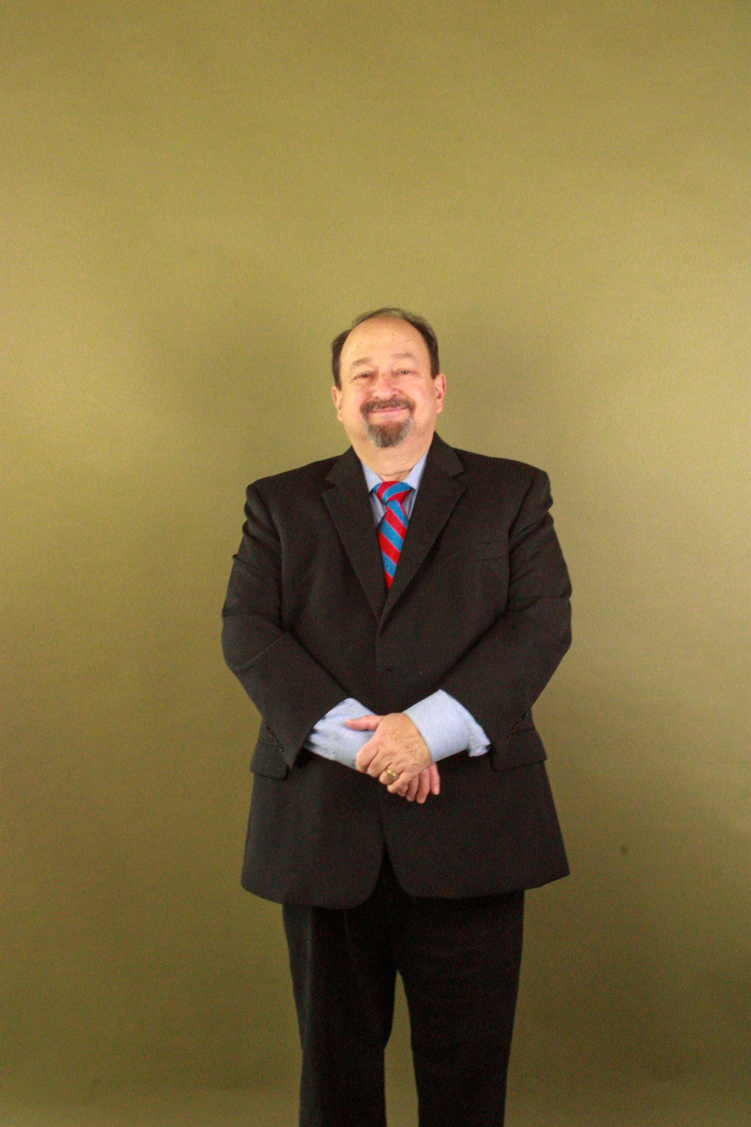 Professional wearing a dark business suit and red tie poses in a series of expressive body language stances against beige wall.