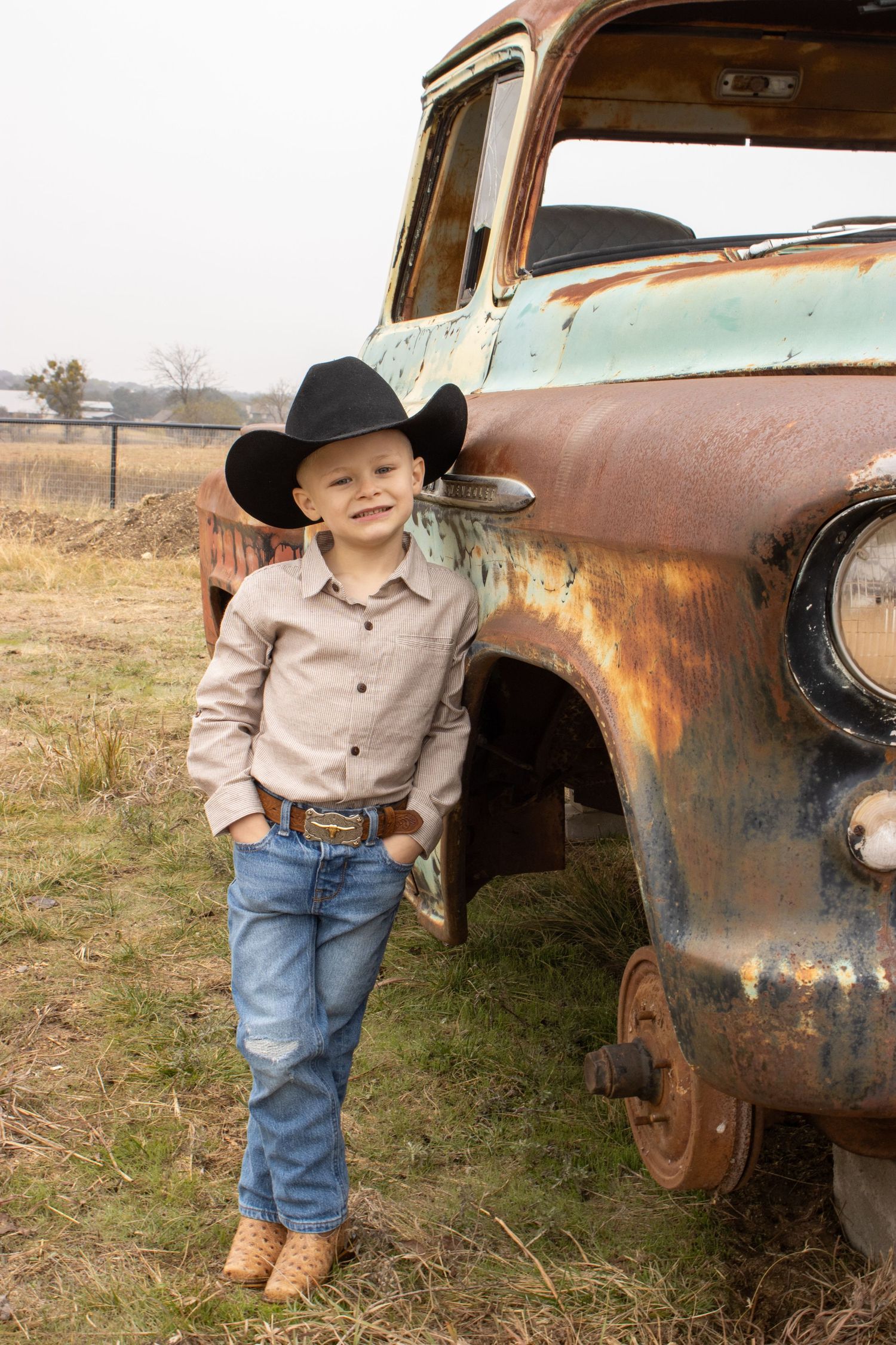 A vintage-themed portrait session with a rustic abandoned car in a rural field setting.