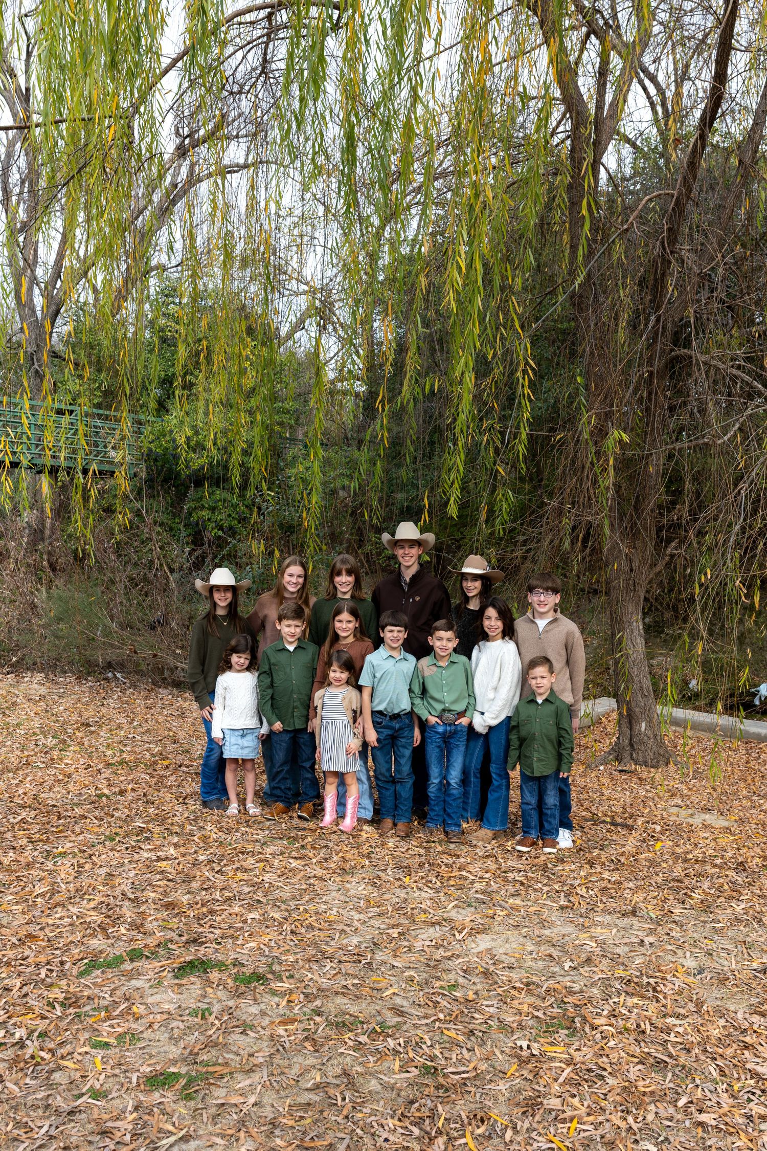 A group stands together outdoors against a backdrop of willow trees and fallen autumn leaves.