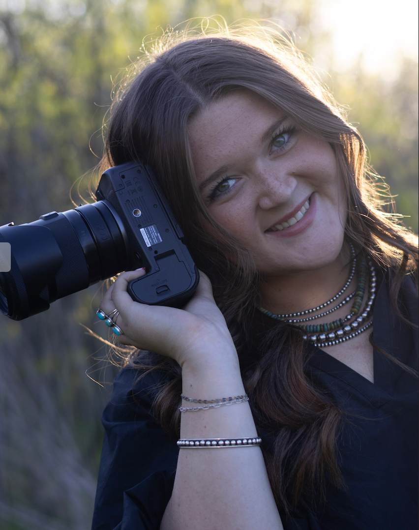 A photographer with long dark hair wearing a black top and necklace poses with a camera in various angles outdoors.