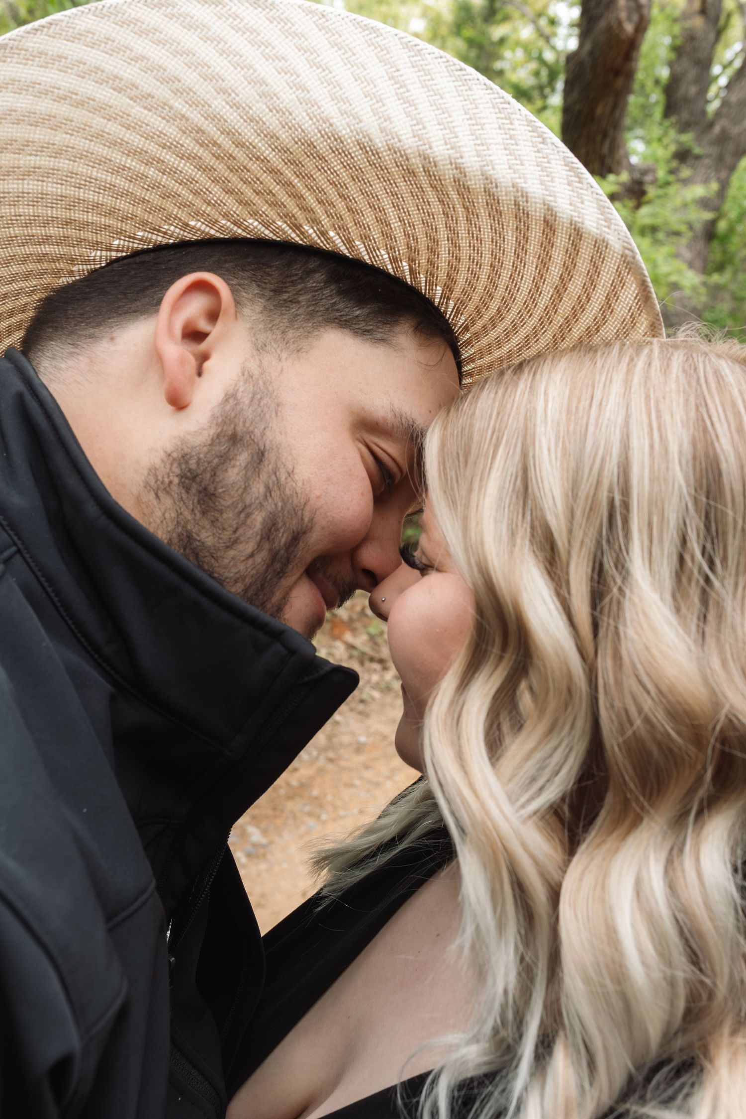 A couple in casual attire sharing tender moments against a natural outdoor background.