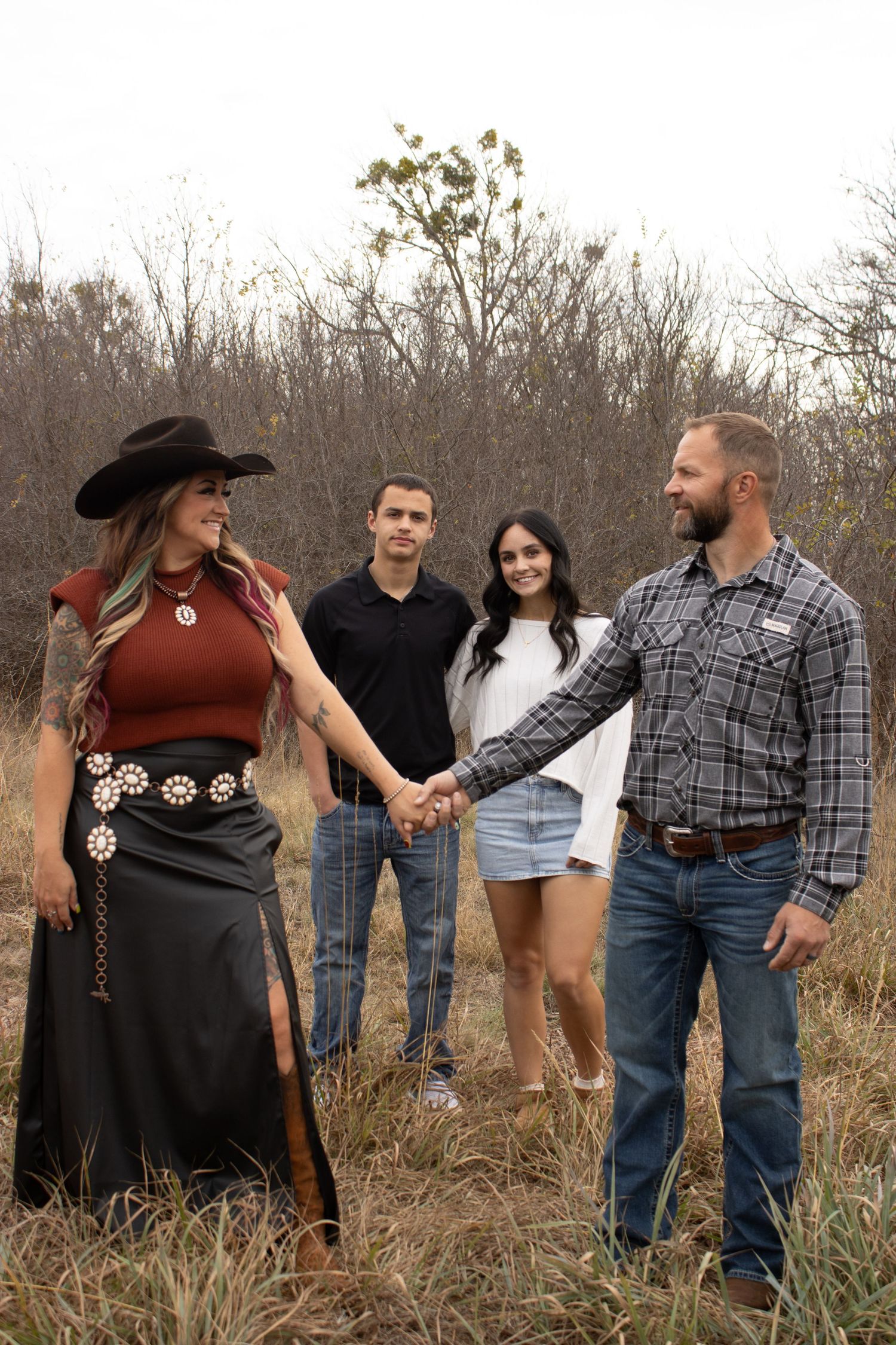 A group of people in western attire pose together in a field of tall grass during autumn.