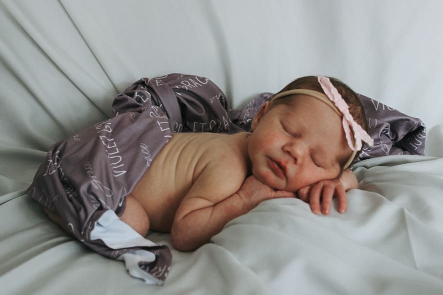 A sleeping baby wearing a gray outfit on white bedding.