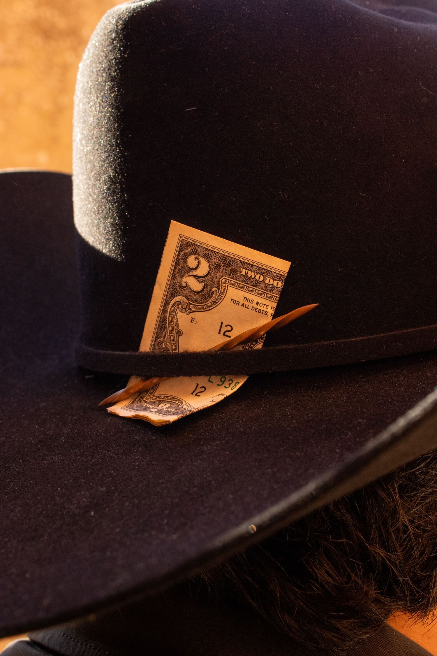 A black cowboy hat with paper money tucked into the band, photographed against a warm background.