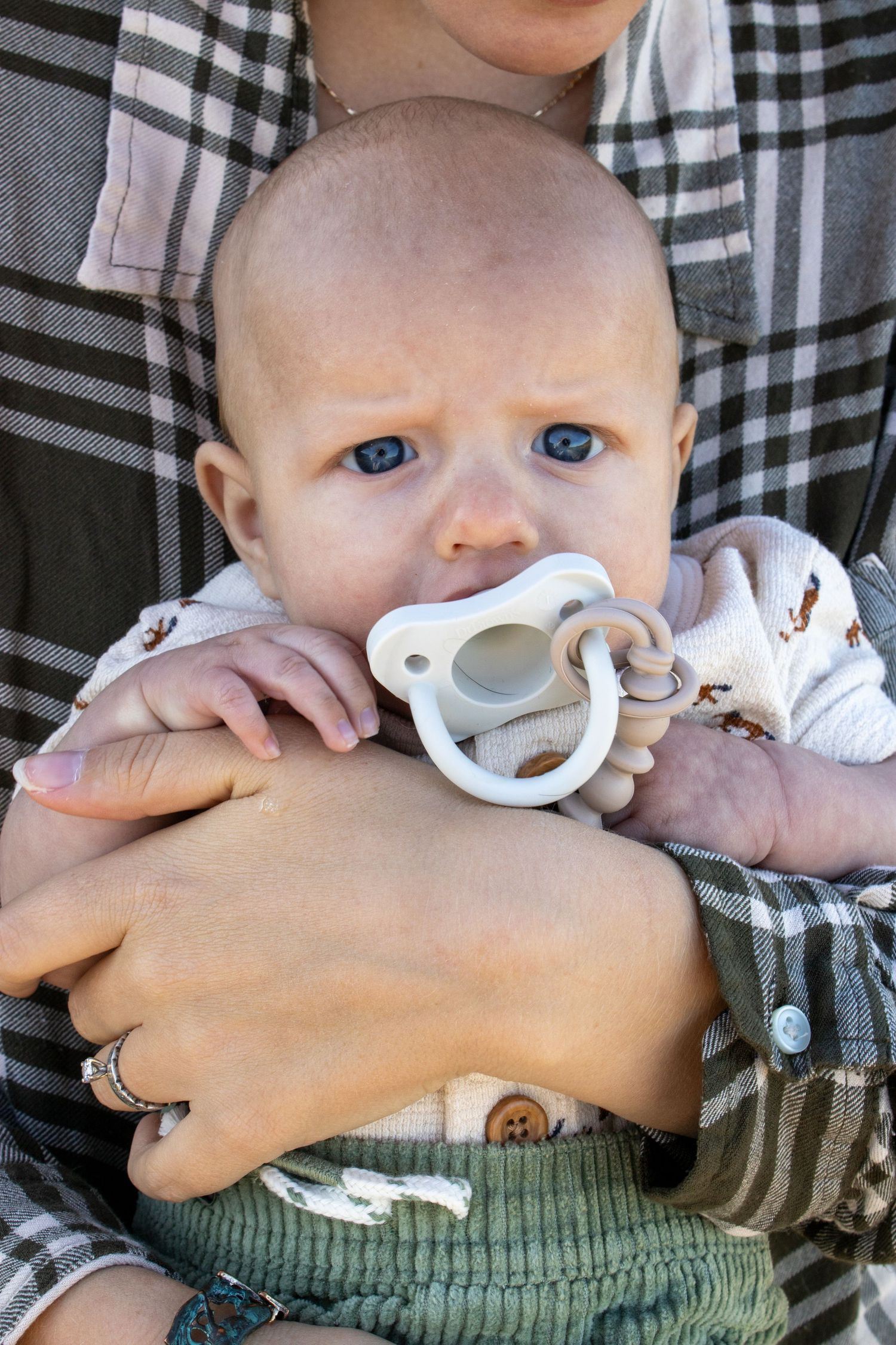 A series of close-up photos showing a baby's face and hands with a white pacifier against a plaid background.