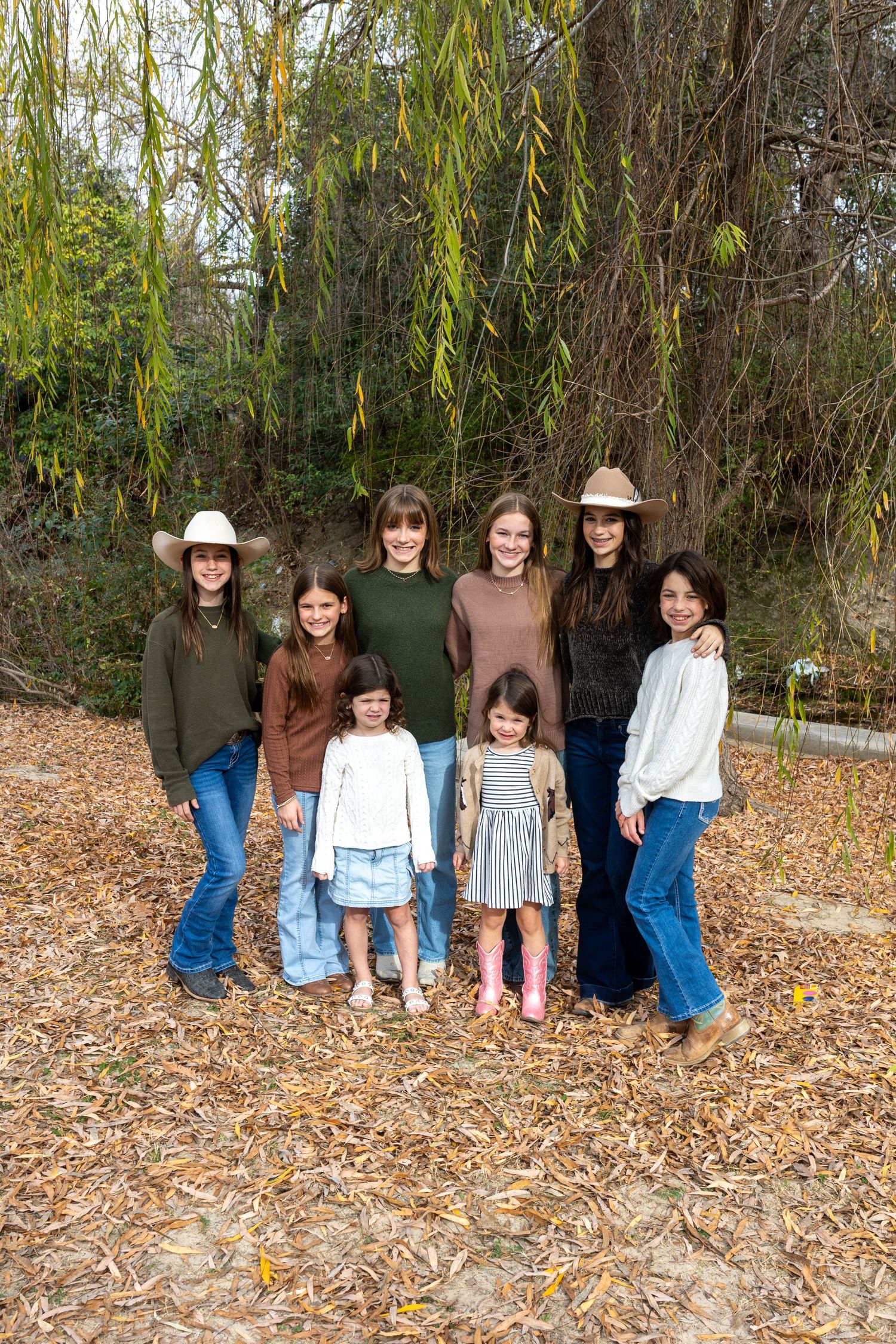 A group sitting together on fallen autumn leaves against a backdrop of trees and greenery.
