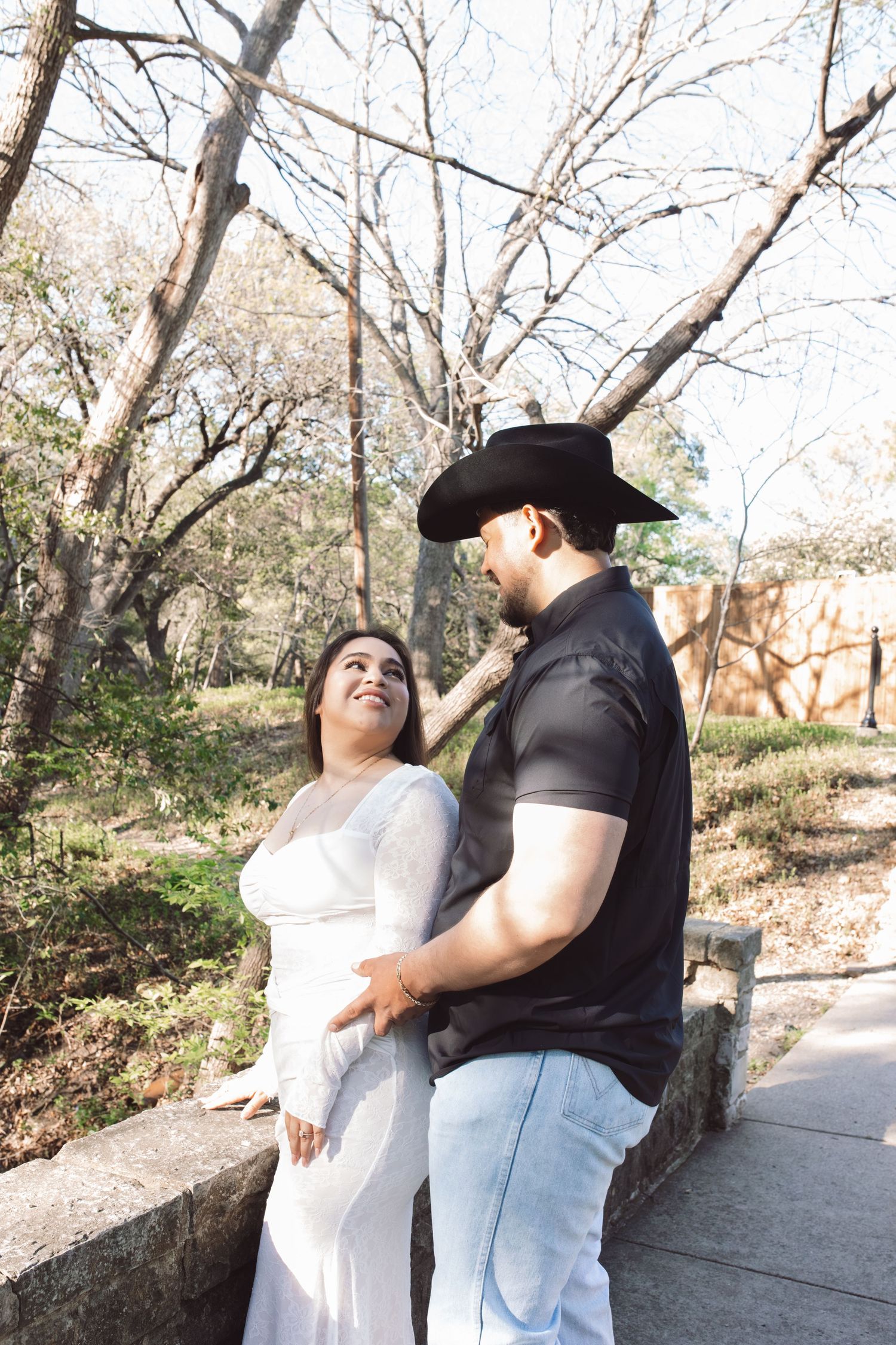 A couple shares a tender moment outdoors, with the man wearing a black cowboy hat and casual attire.