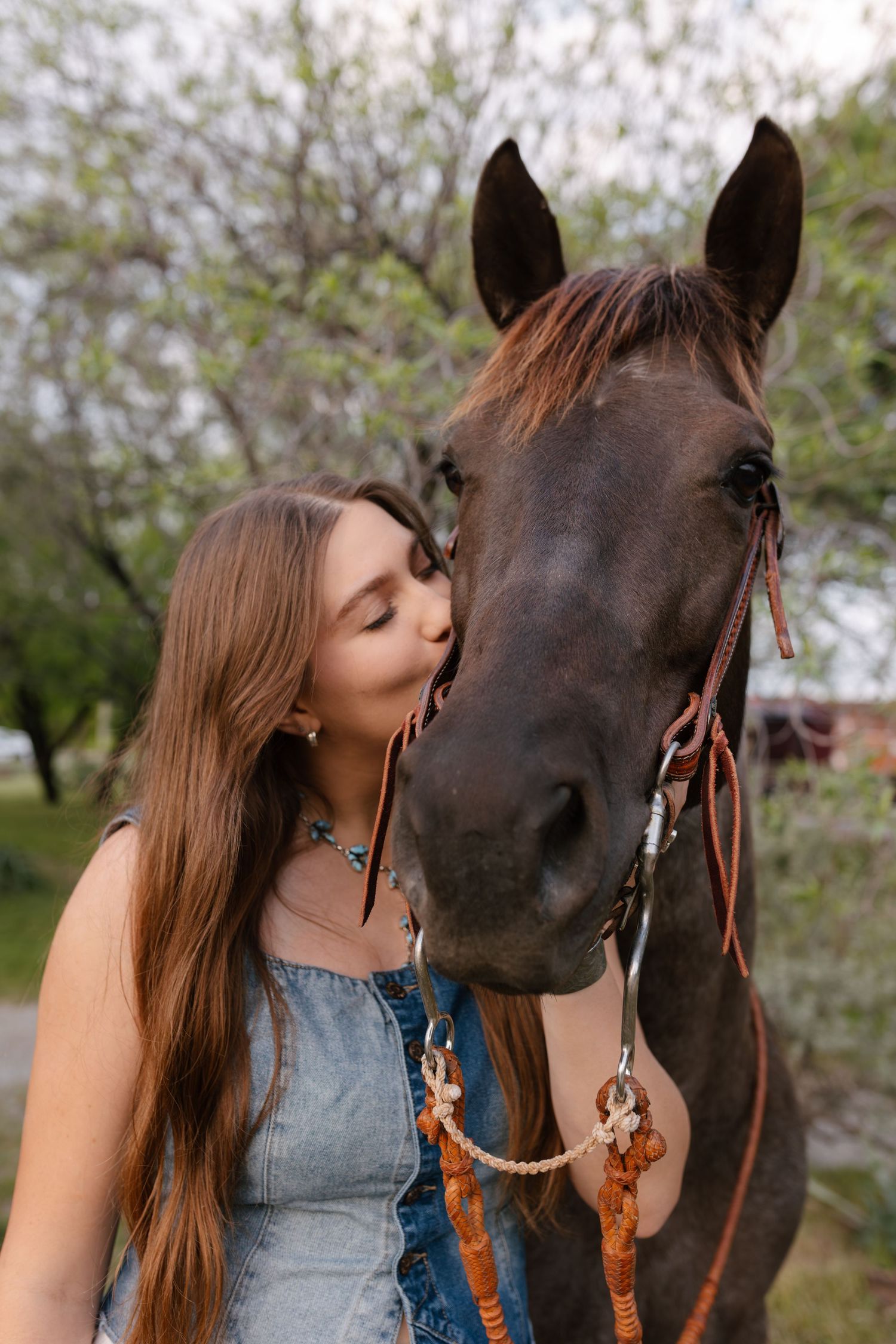 A woman in a denim top shares tender moments with a dark brown horse against a spring blossom backdrop.