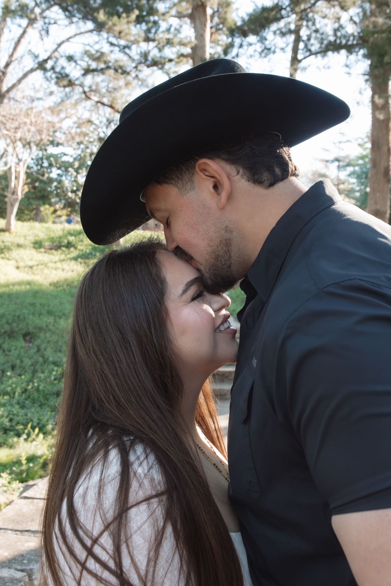 A romantic outdoor portrait of a couple sharing an intimate moment among trees.