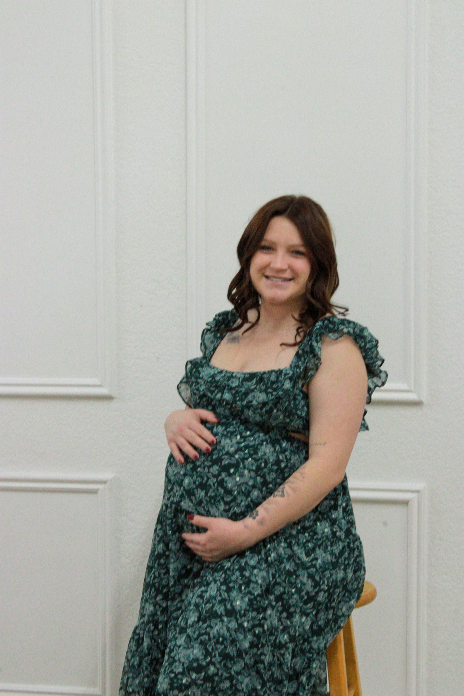 Woman in a green floral dress poses in different positions against a white wall.