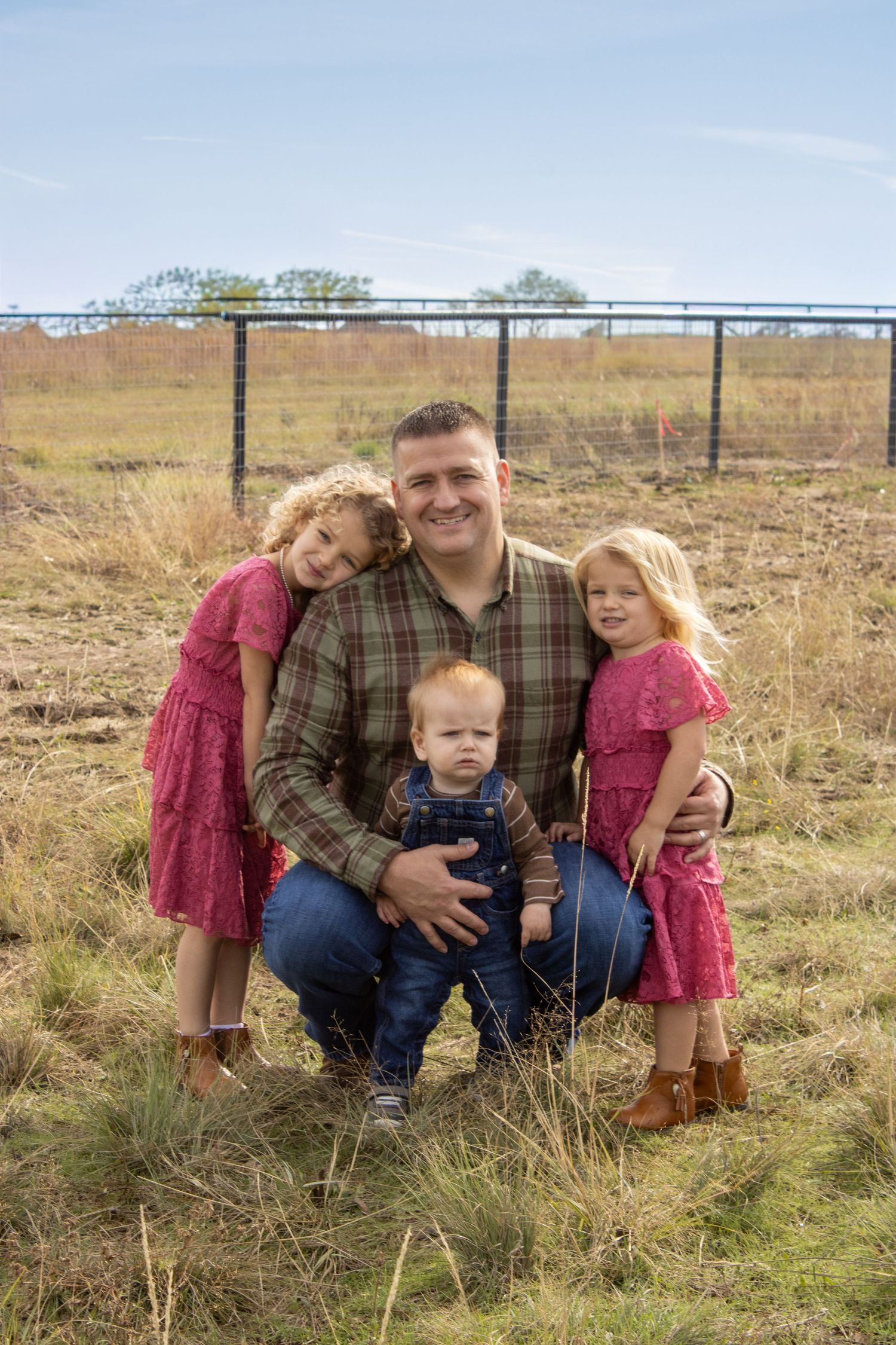 A family in casual attire poses together on grassy farmland during a sunny autumn day.