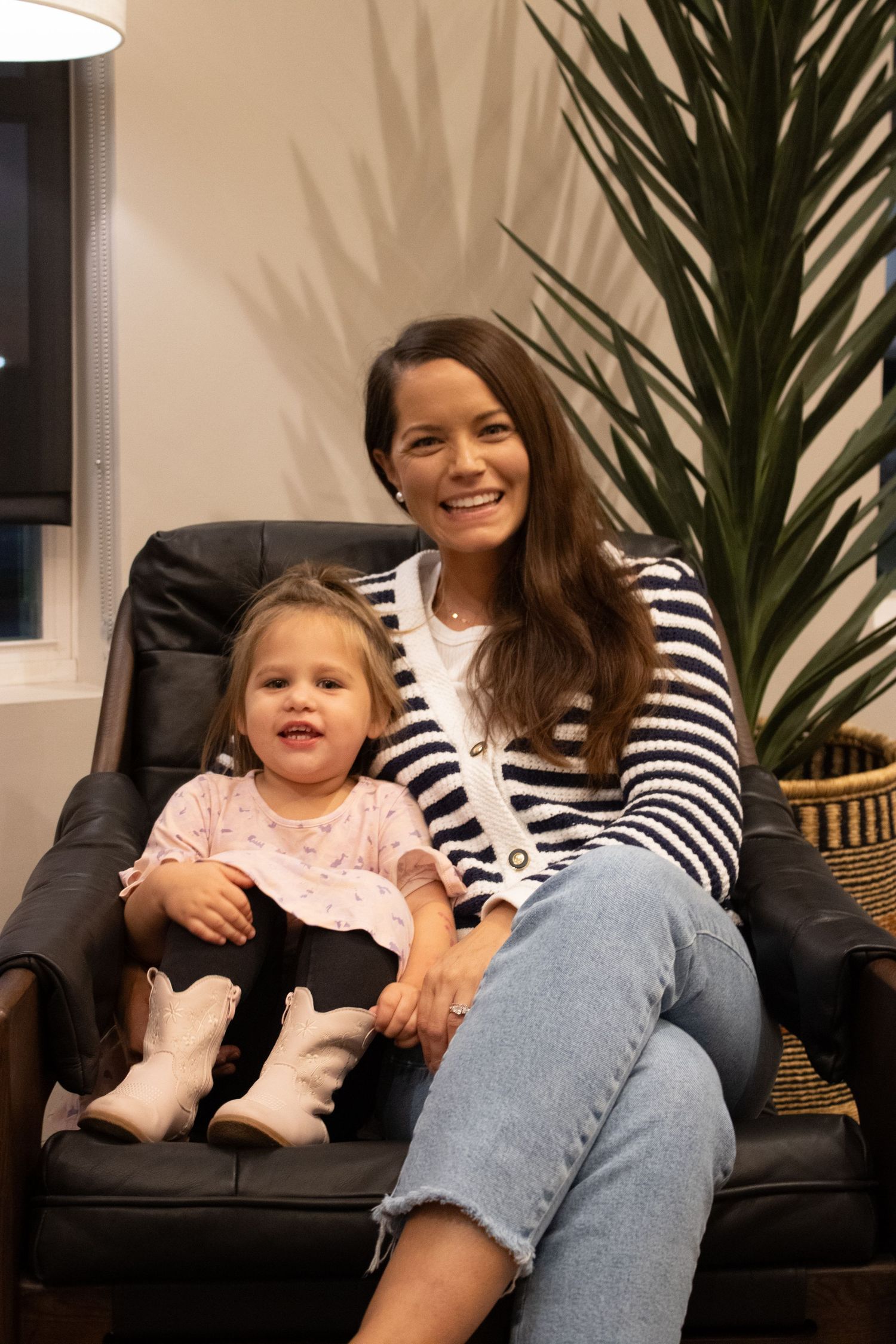 A cozy indoor portrait of two people sitting together on a black leather chair near a large houseplant.