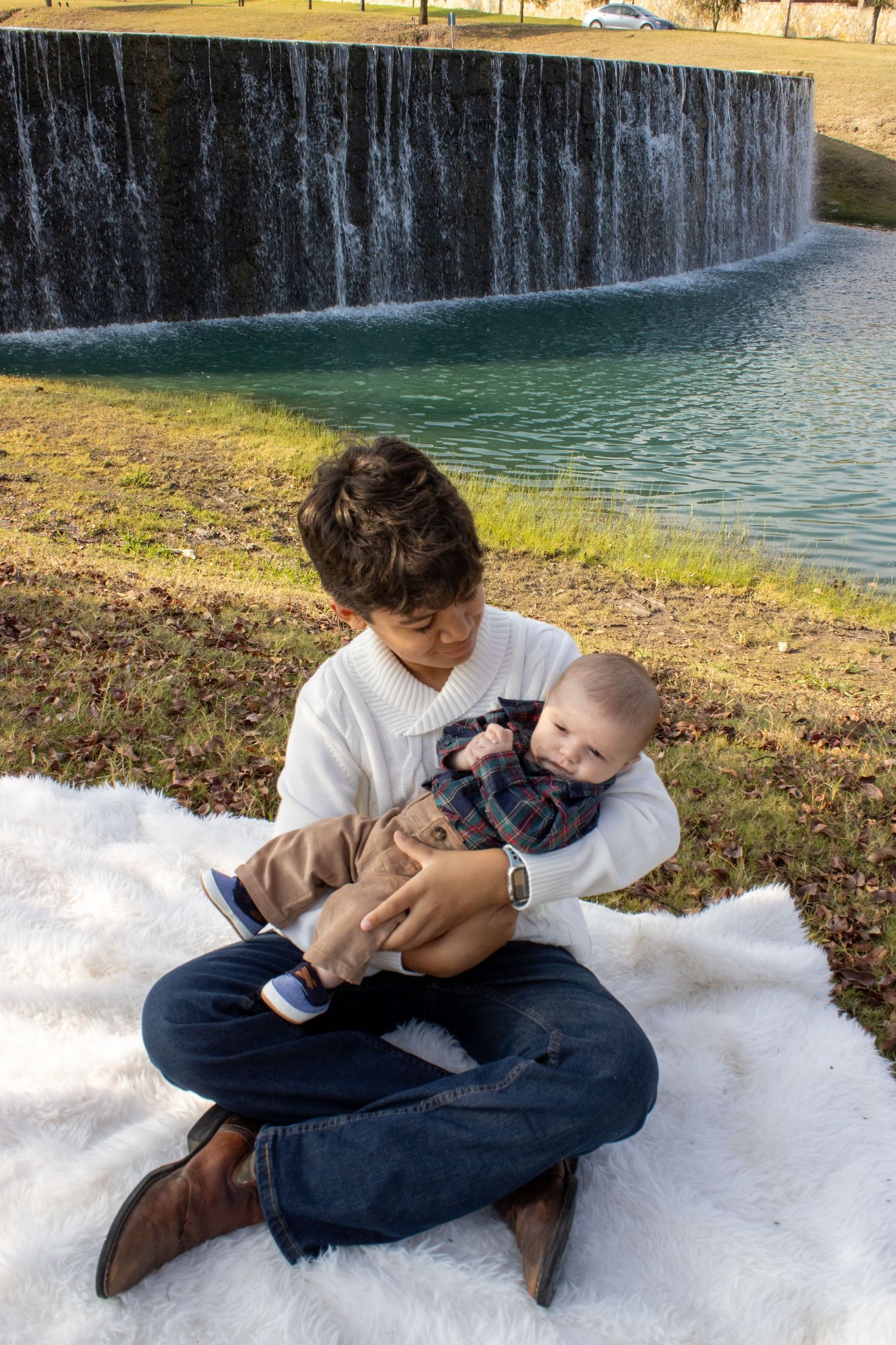 Two children playing together on a snowy patch of ground near a waterfall on a sunny winter day.