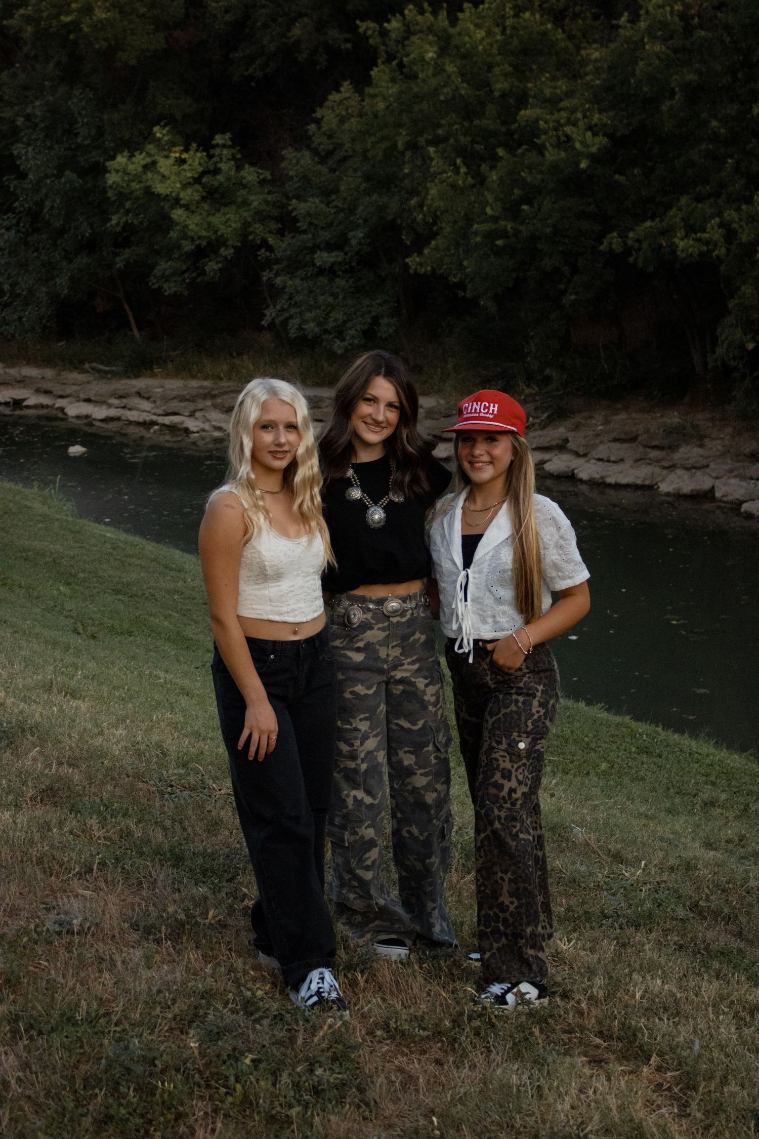 Friends in casual outfits posing together by a lake.