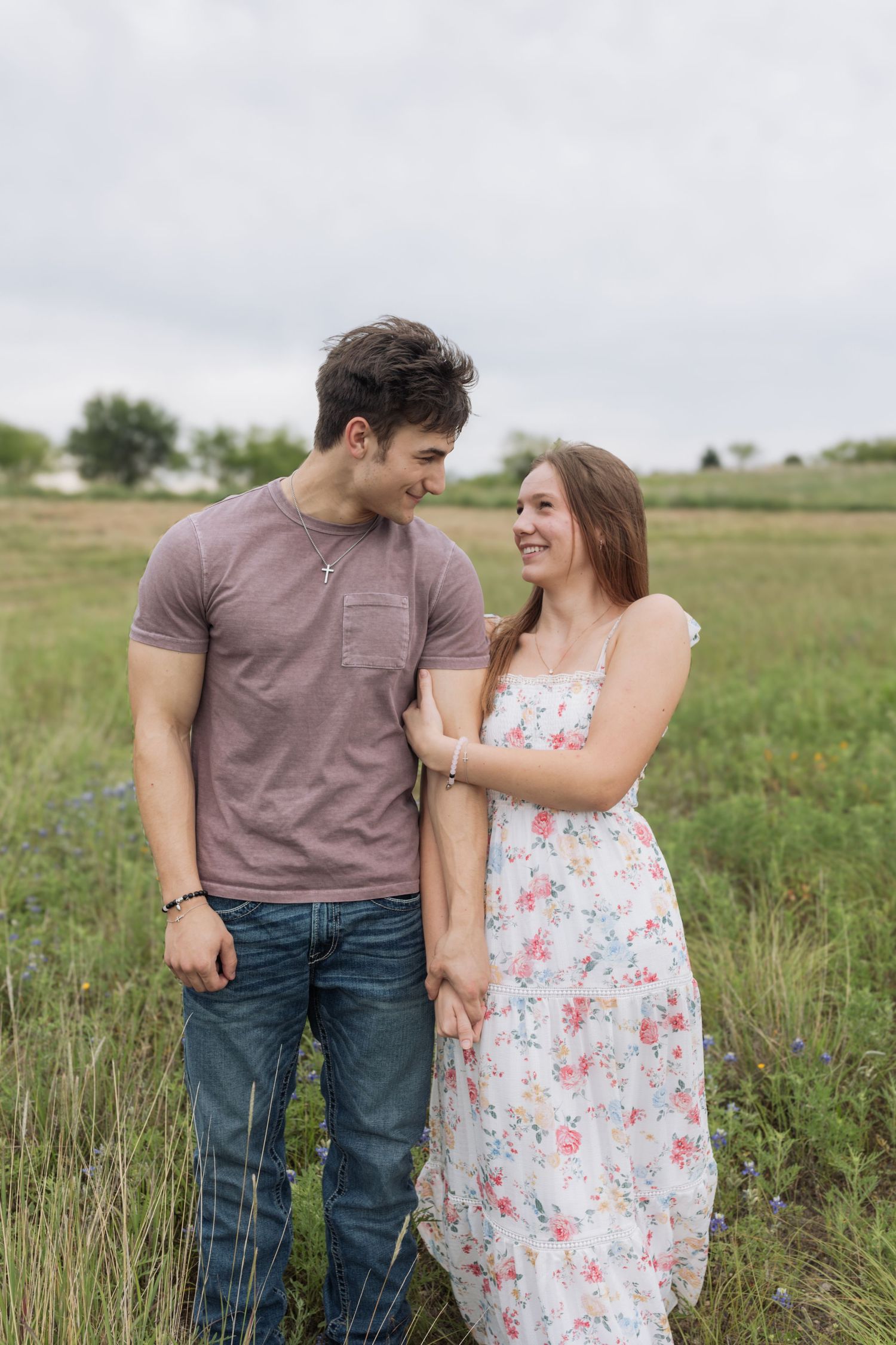 Happy young couple holds hands and smiles at each other in a lush green field.