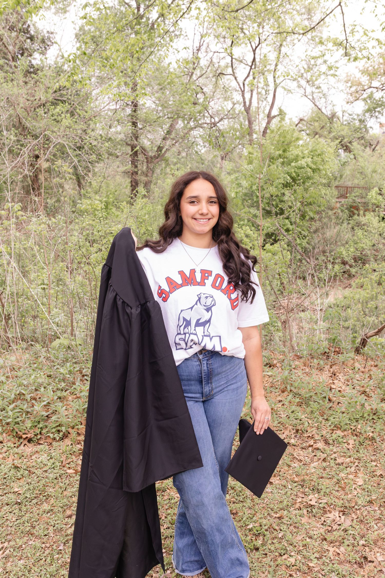 Casual outdoor photoshoot featuring high-waisted jeans, graphic t-shirt, and black blazer against natural foliage.