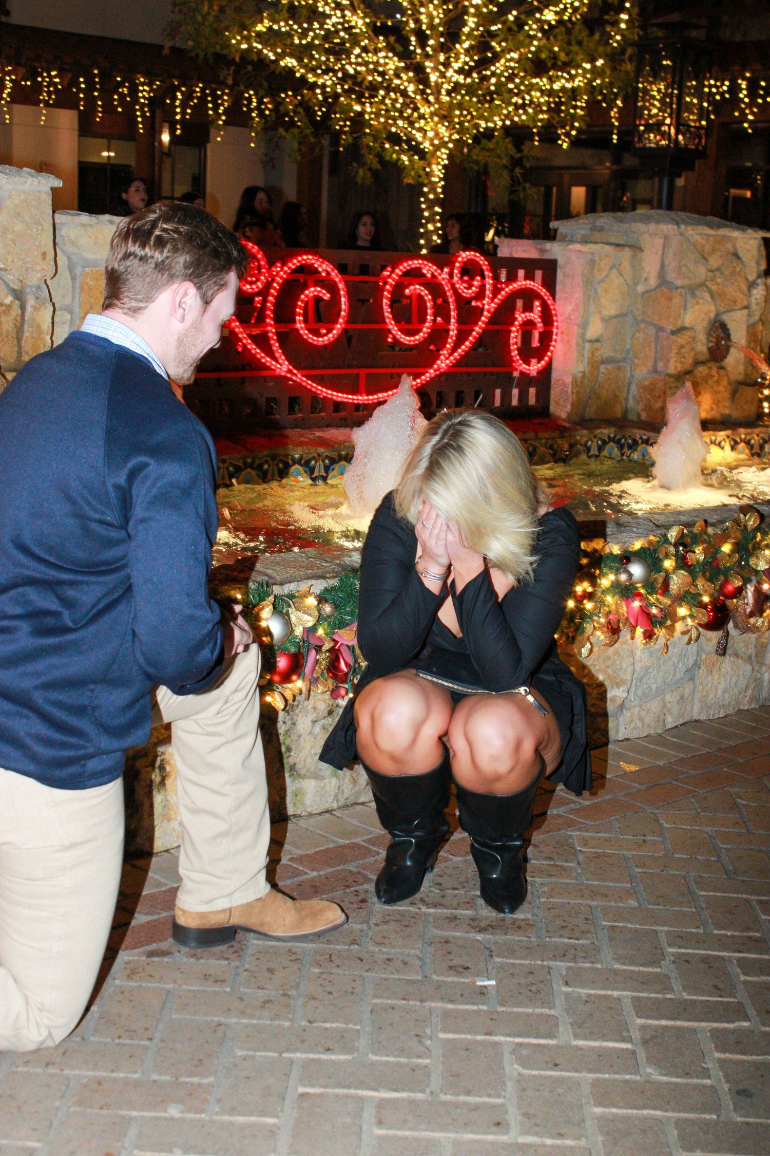 A couple poses on brick steps decorated with holiday lights and festive decorations.