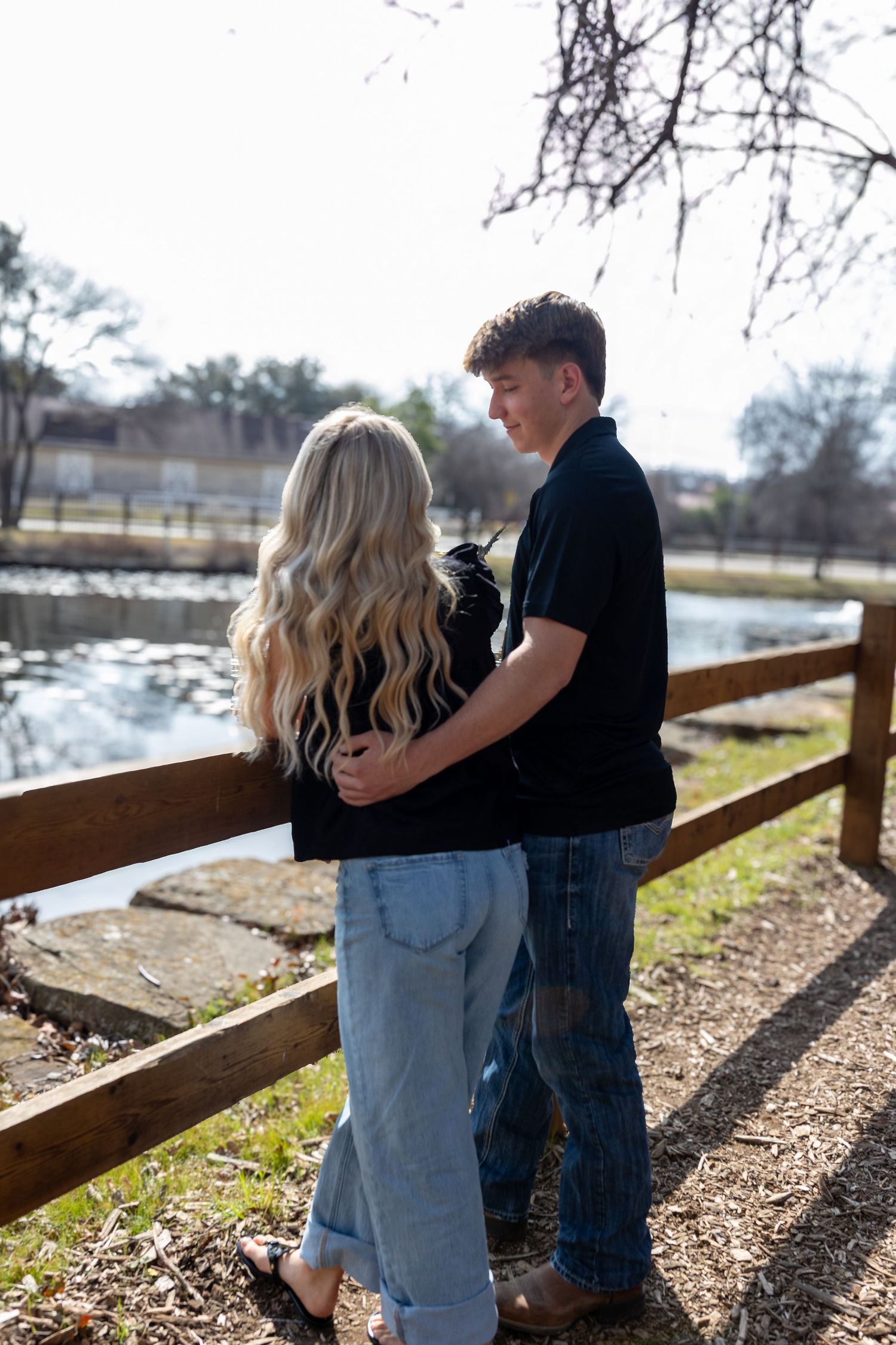A couple enjoys a peaceful moment overlooking a lake from a wooden bridge.