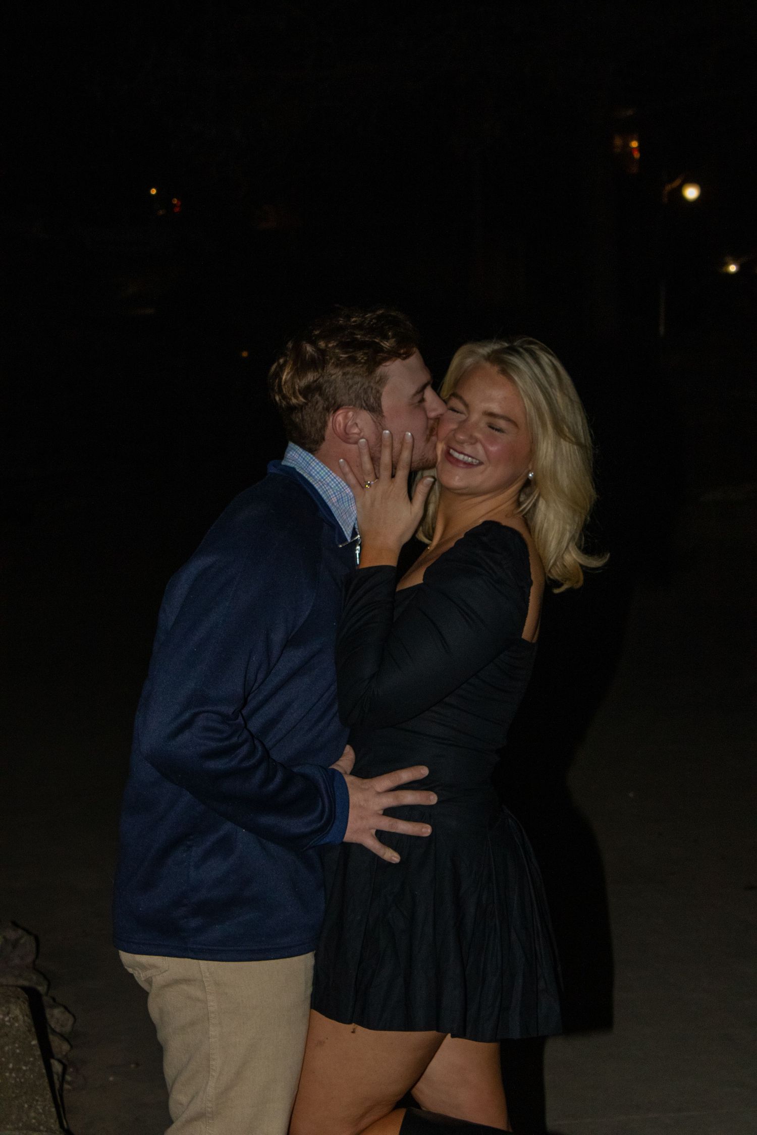 A couple shares a romantic moment outdoors at night in a casual setting.
