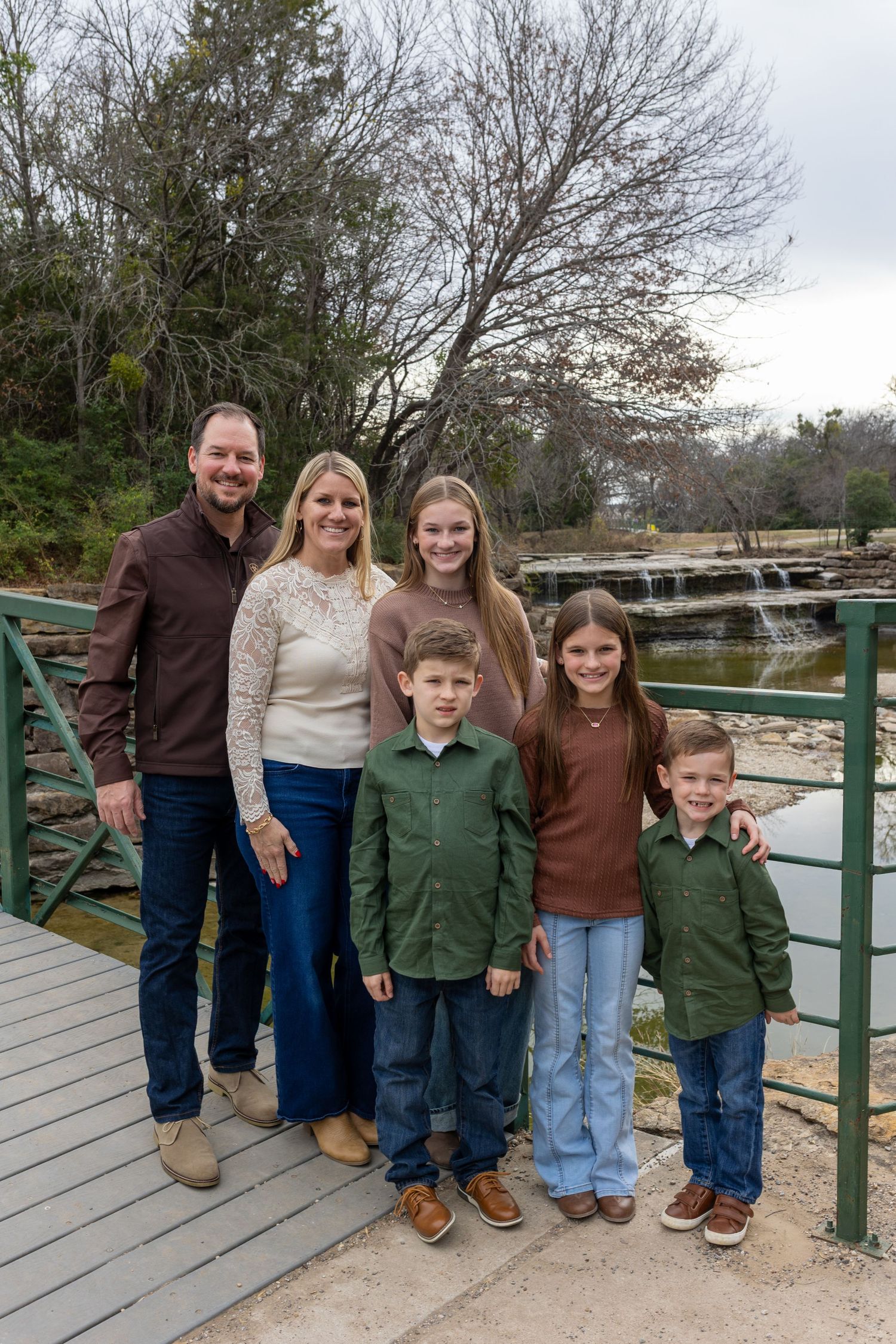 A group stands together on a wooden deck overlooking a waterfall on an overcast day.